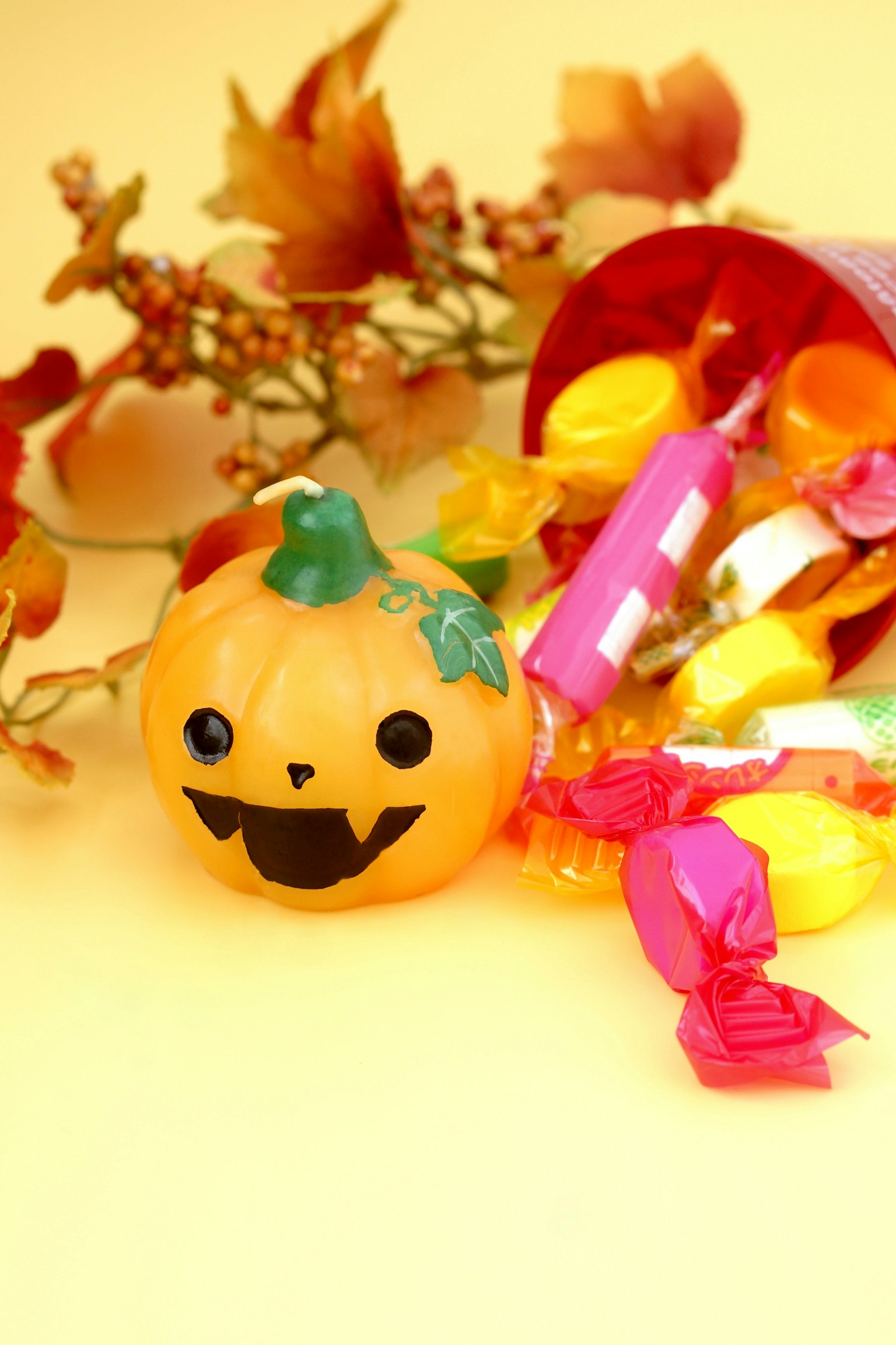 Une décoration de citrouille orange souriante entourée de bonbons colorés et de feuilles d'automne