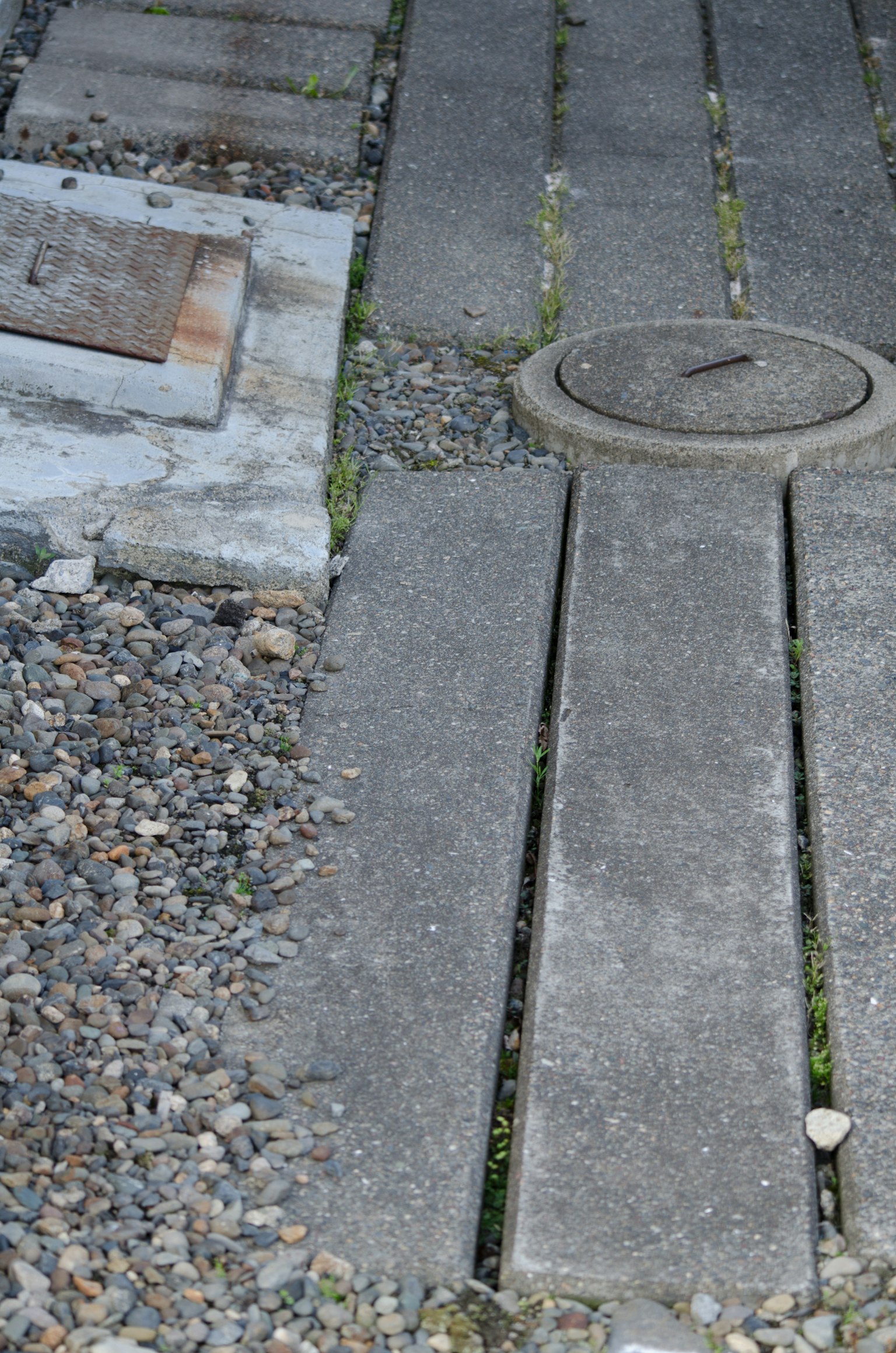 Betonplatten mit einem Kanalschacht auf einem Kiesweg