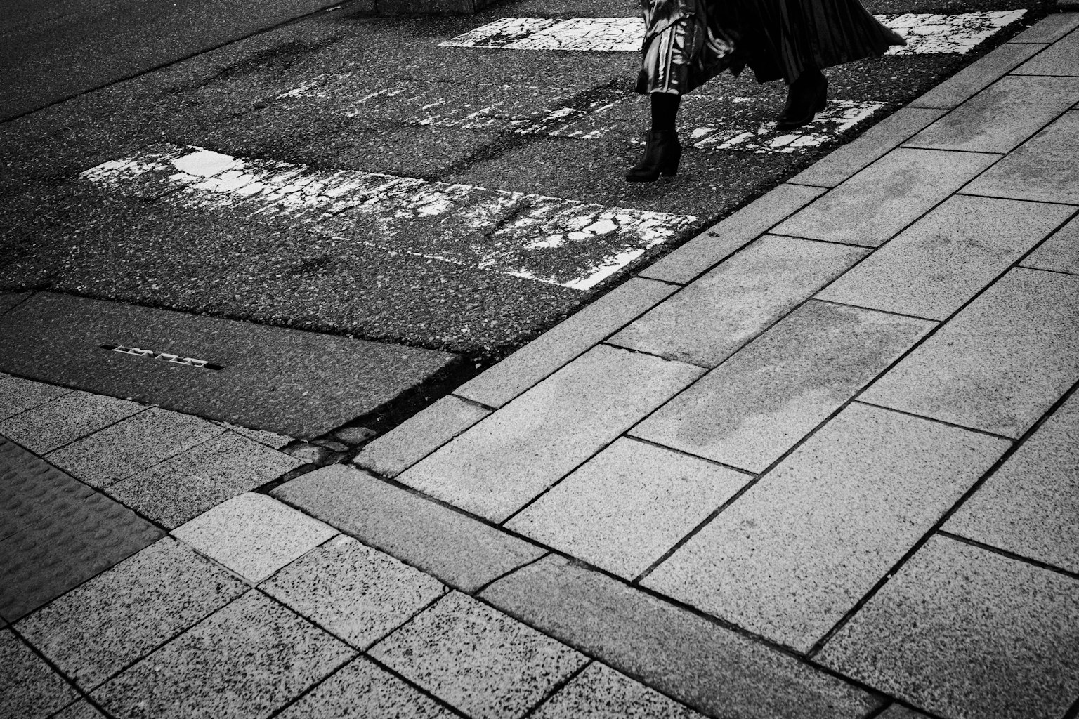 Escena de calle en blanco y negro con los pies de una persona en un paso de peatones