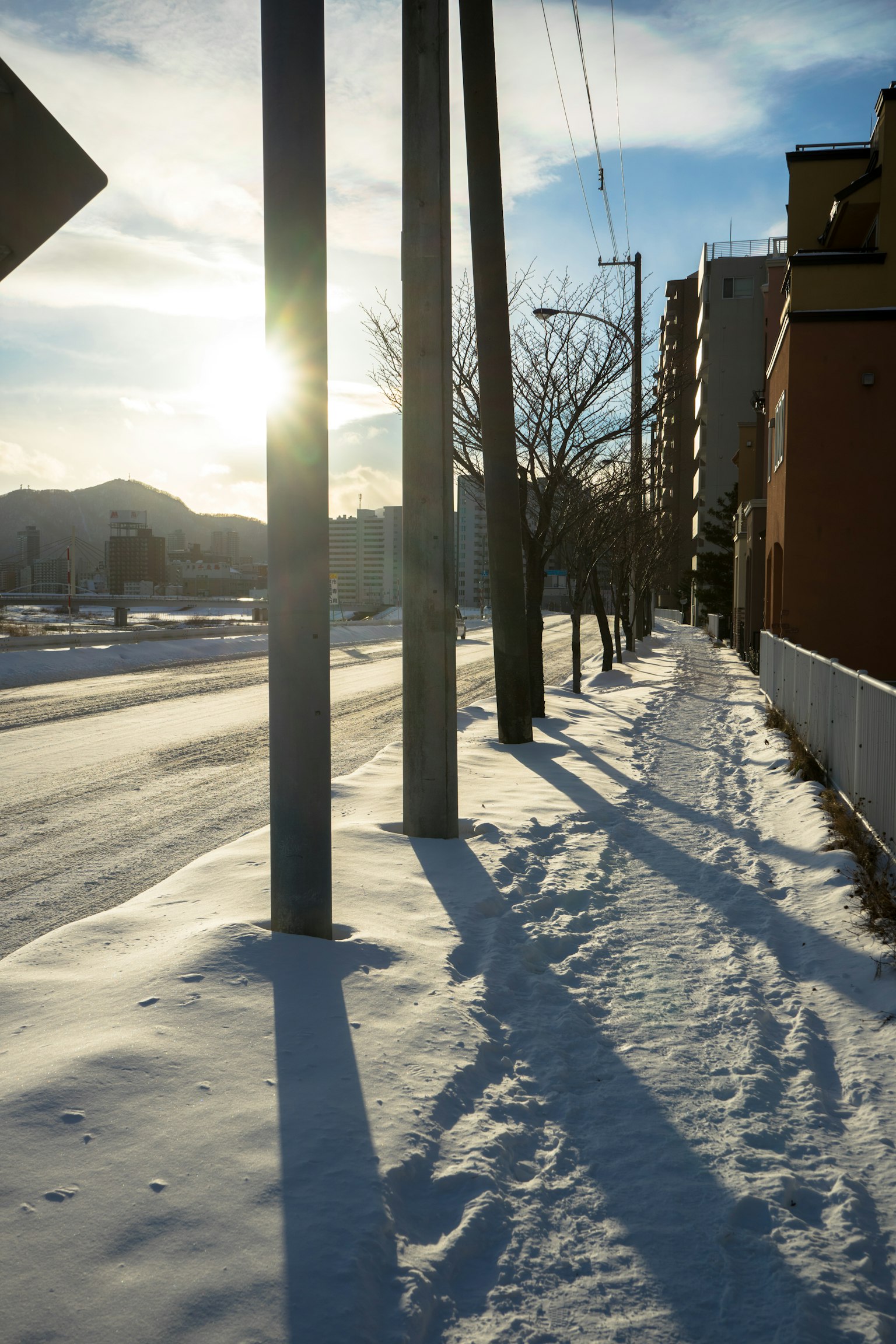 Snow-covered sidewalk with long shadows and urban scenery