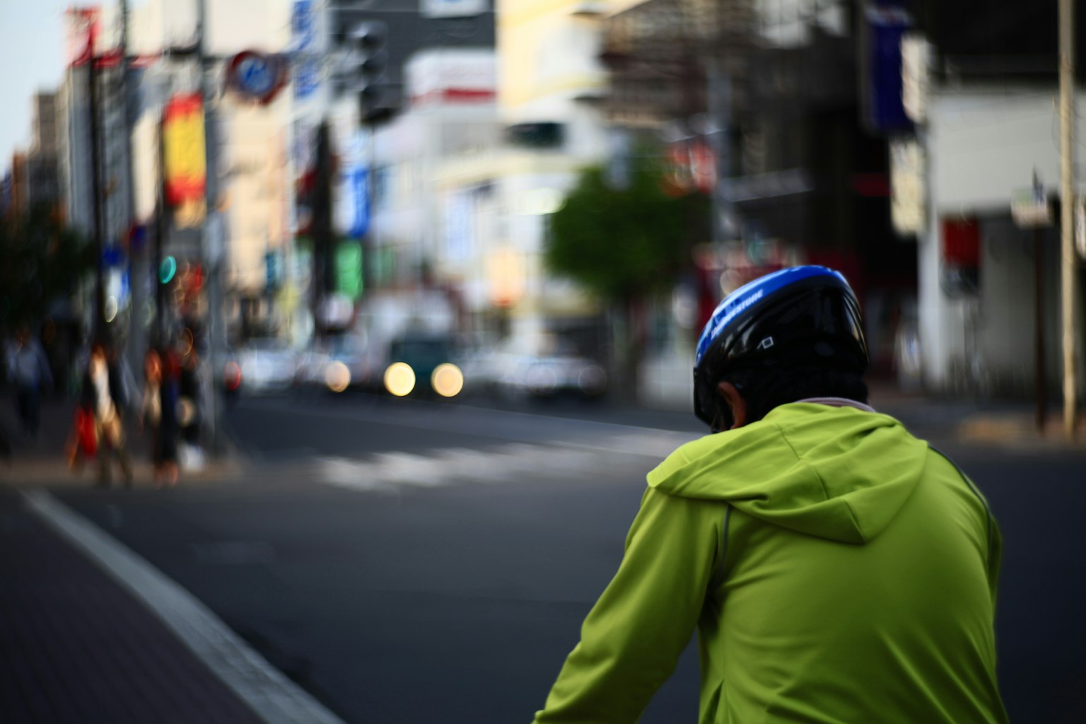 A cyclist wearing a bright yellow jacket and helmet with a blurred city background