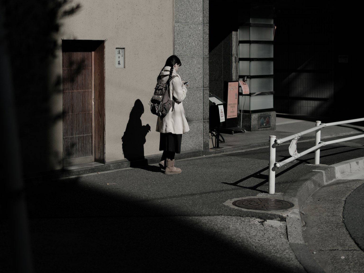 Eine Frau steht an einer Straßenecke und schaut auf ihr Smartphone mit Schatten