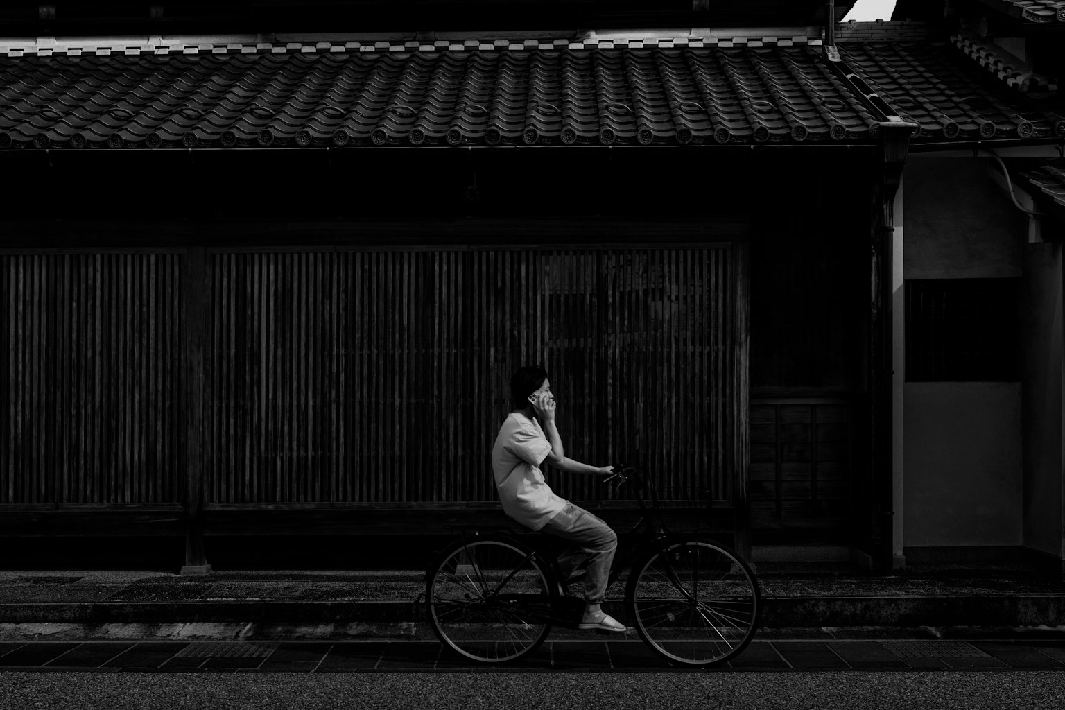 骑自行车的人在黑白色调中，背景是传统日本建筑