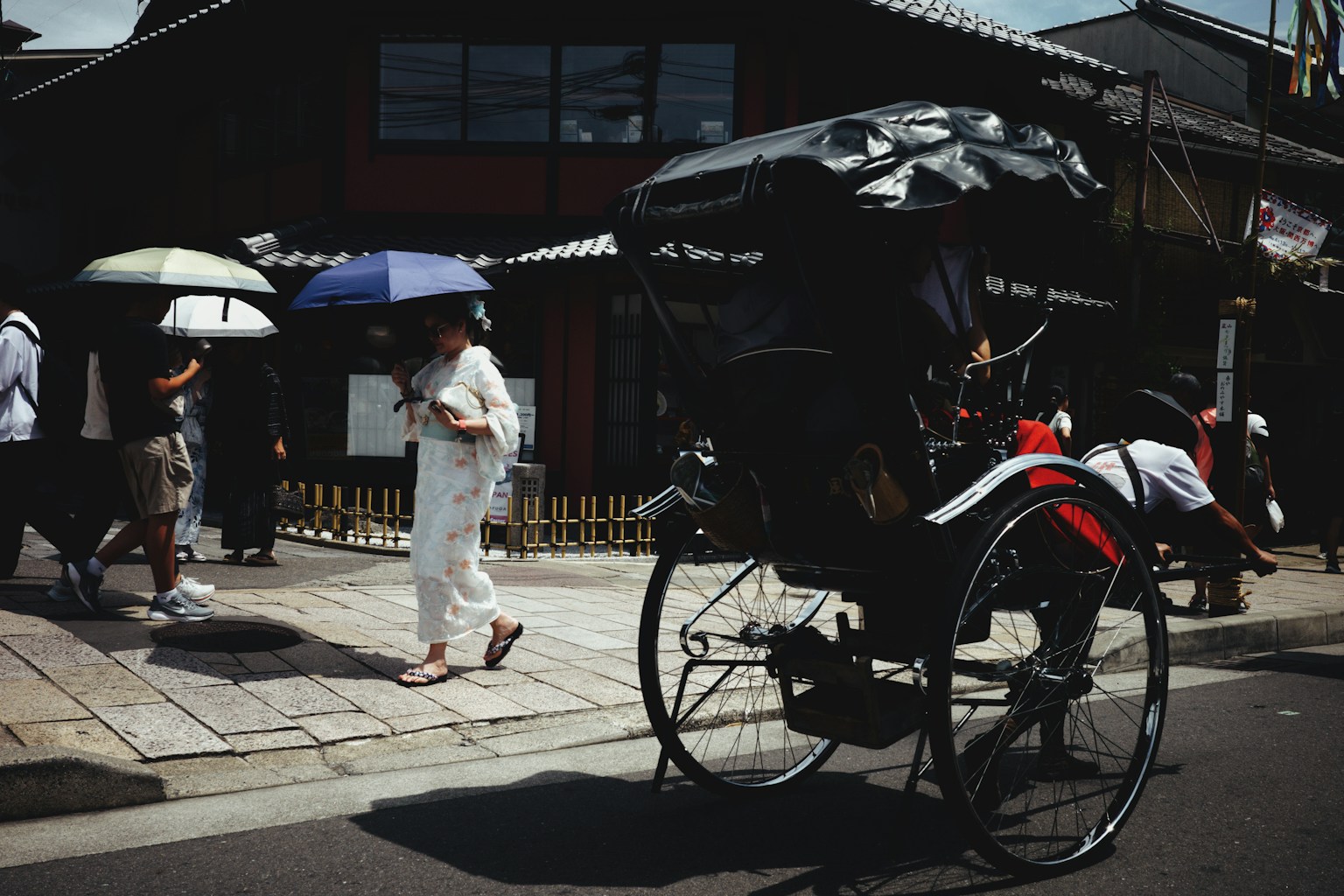 Rickshaw passing by pedestrians with umbrellas in a traditional street