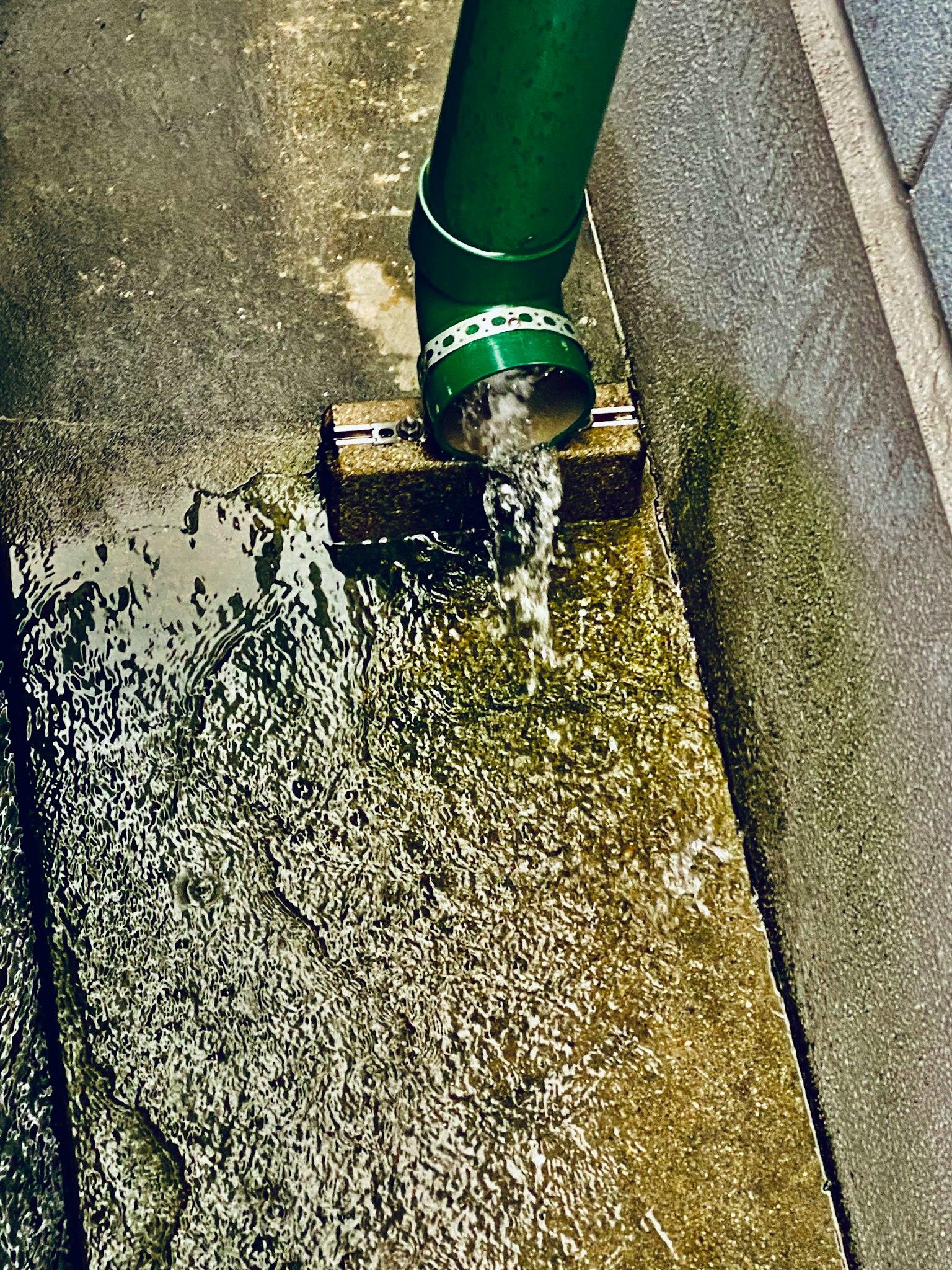 Imagen de agua fluyendo de una tubería verde sobre un suelo de concreto