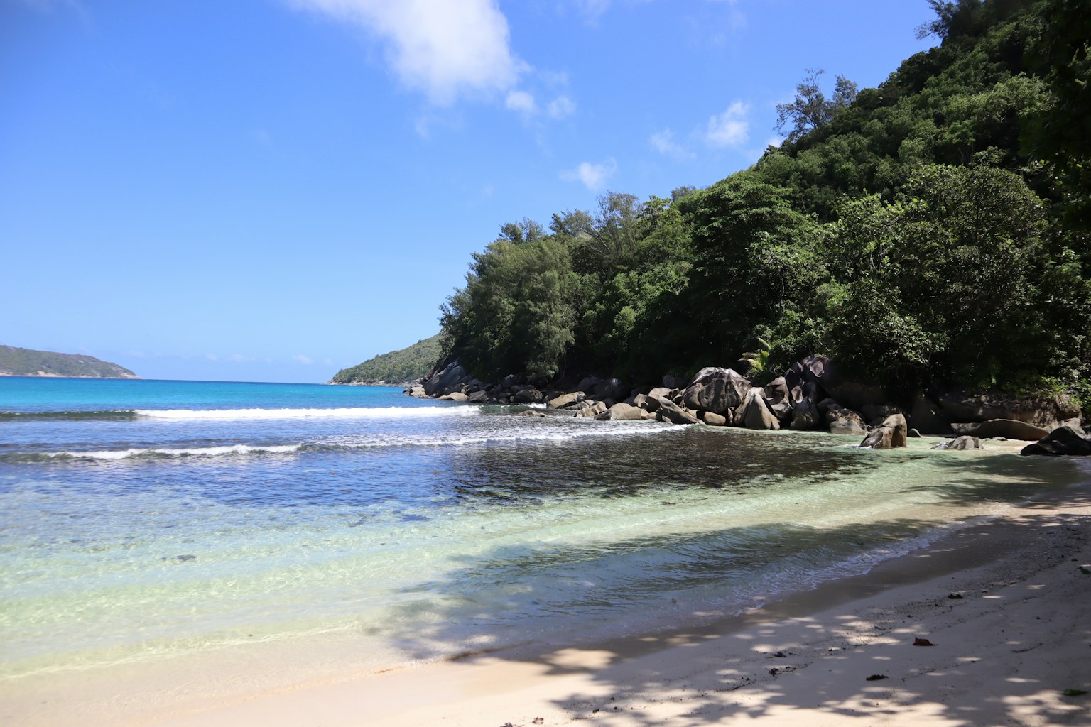 ชายหาดที่มีทัศนียภาพสวยงามมีน้ำทะเลสีเขียวมรกตใสล้อมรอบด้วยพืชพรรณที่เขียวชอุ่มและรูปแบบหิน