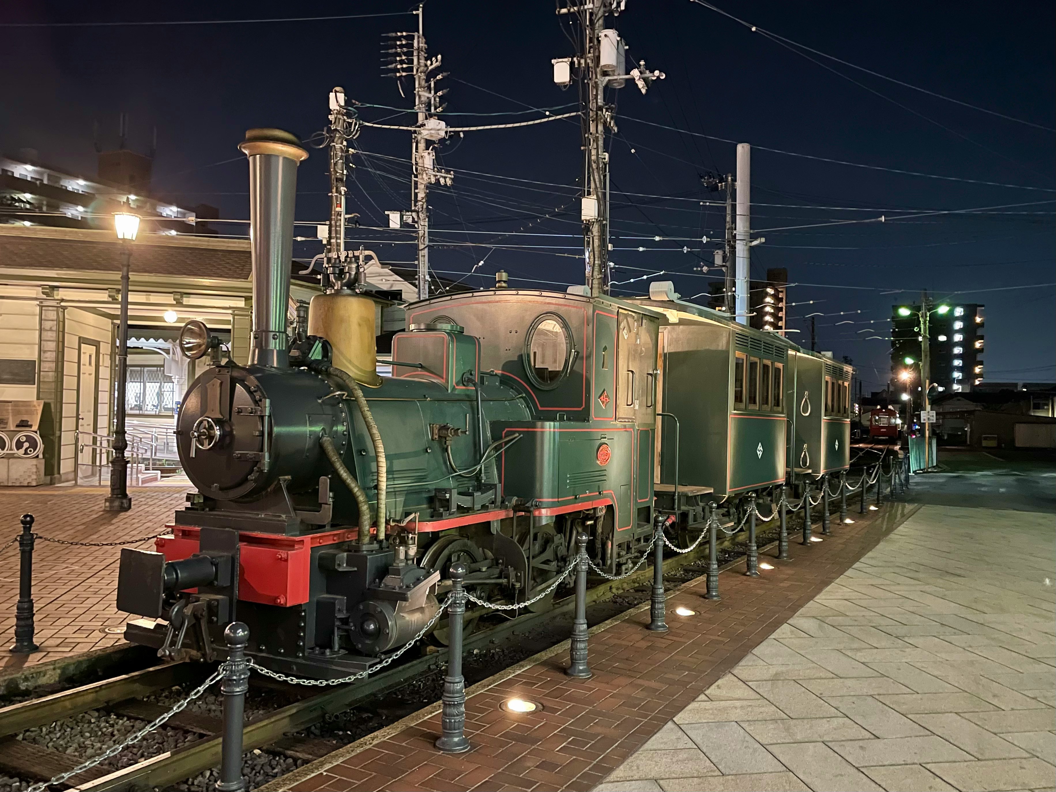 夜の駅前に並ぶ蒸気機関車の展示画像