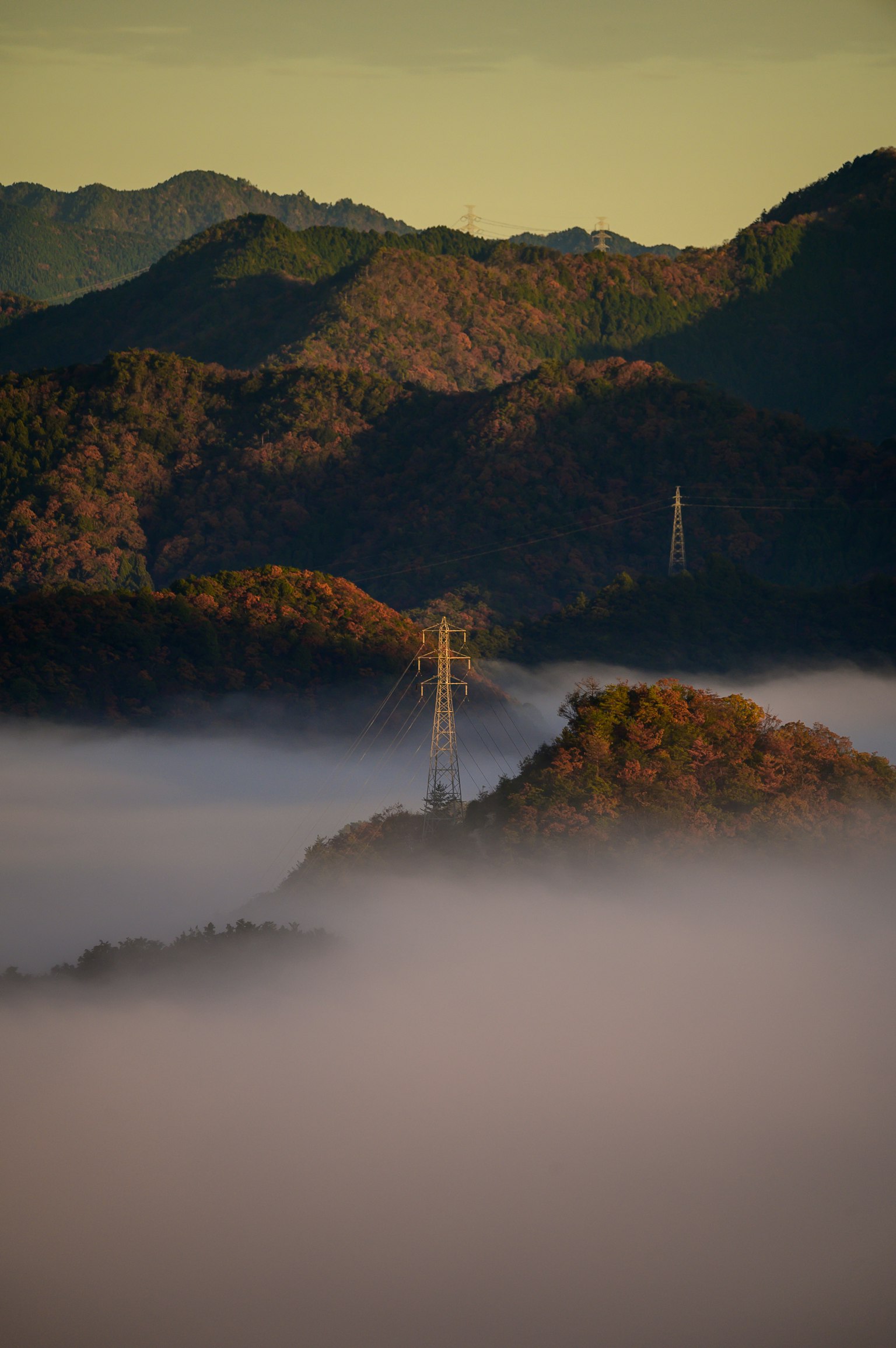Transmission tower emerging from fog with mountains in the background