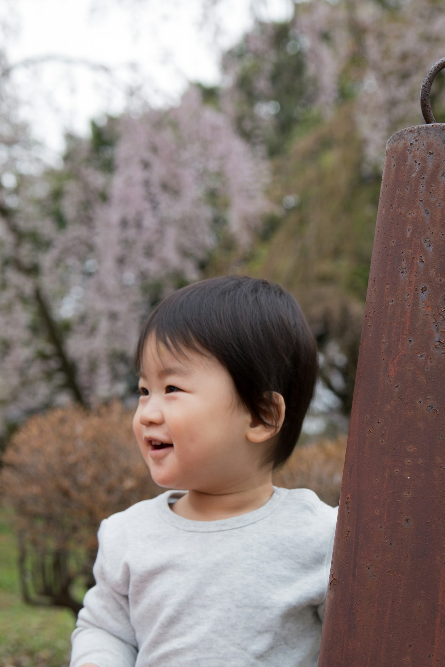Lächelndes Kind steht in einem Park mit Kirschblütenbäumen im Hintergrund