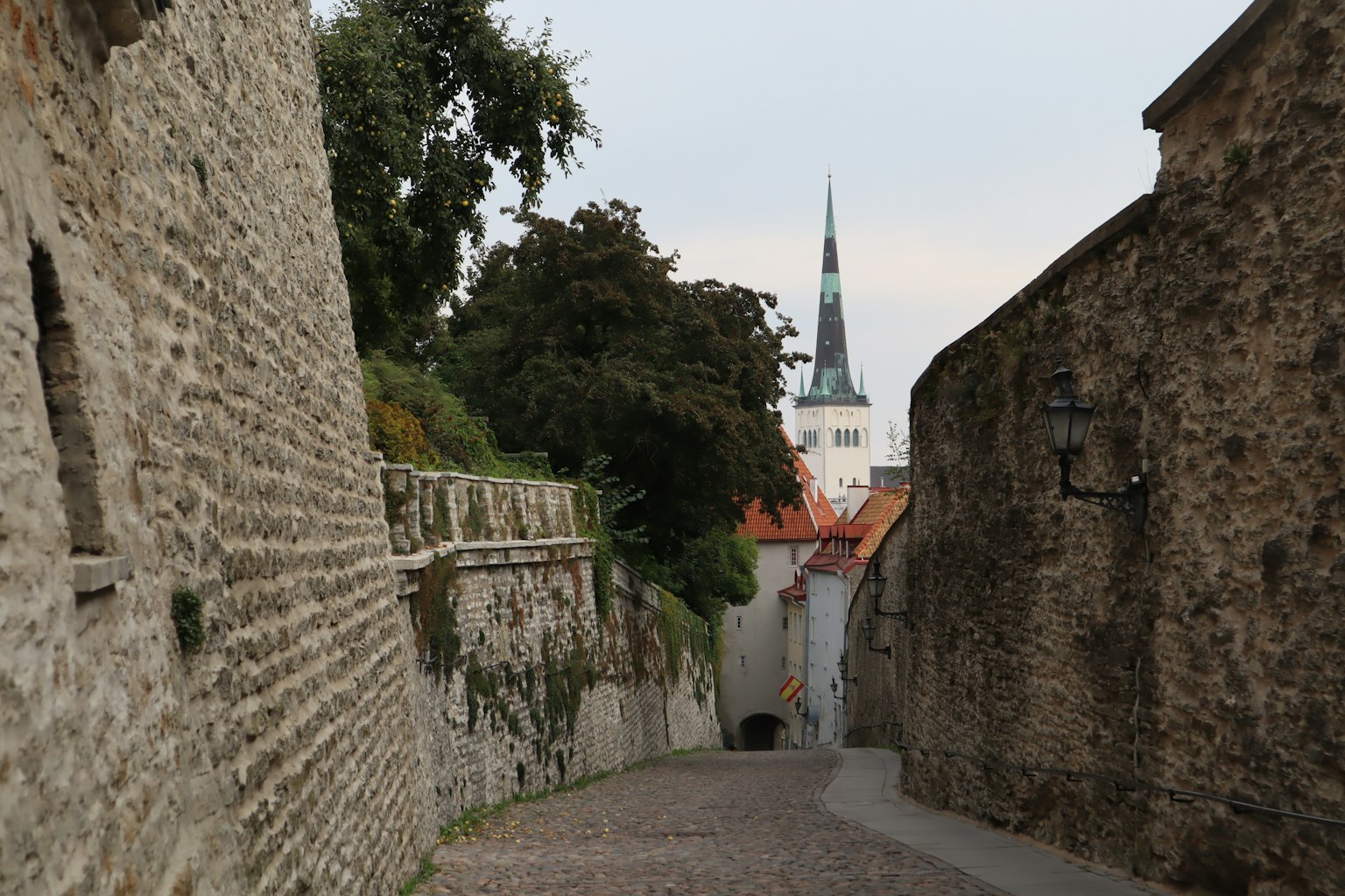 Ruhiger Pflasterweg, flankiert von Steinmauern, mit einem Kirchturm im Hintergrund