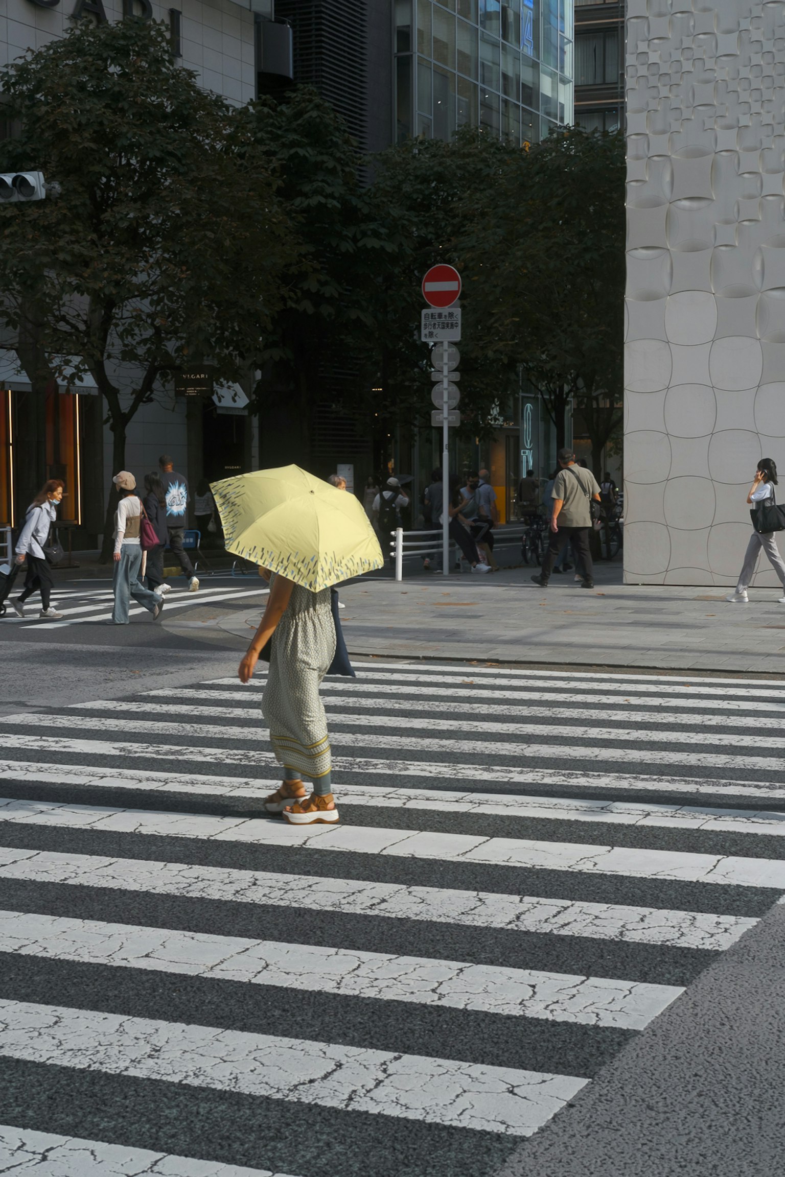 A person with a yellow umbrella crossing a pedestrian crosswalk in an urban setting
