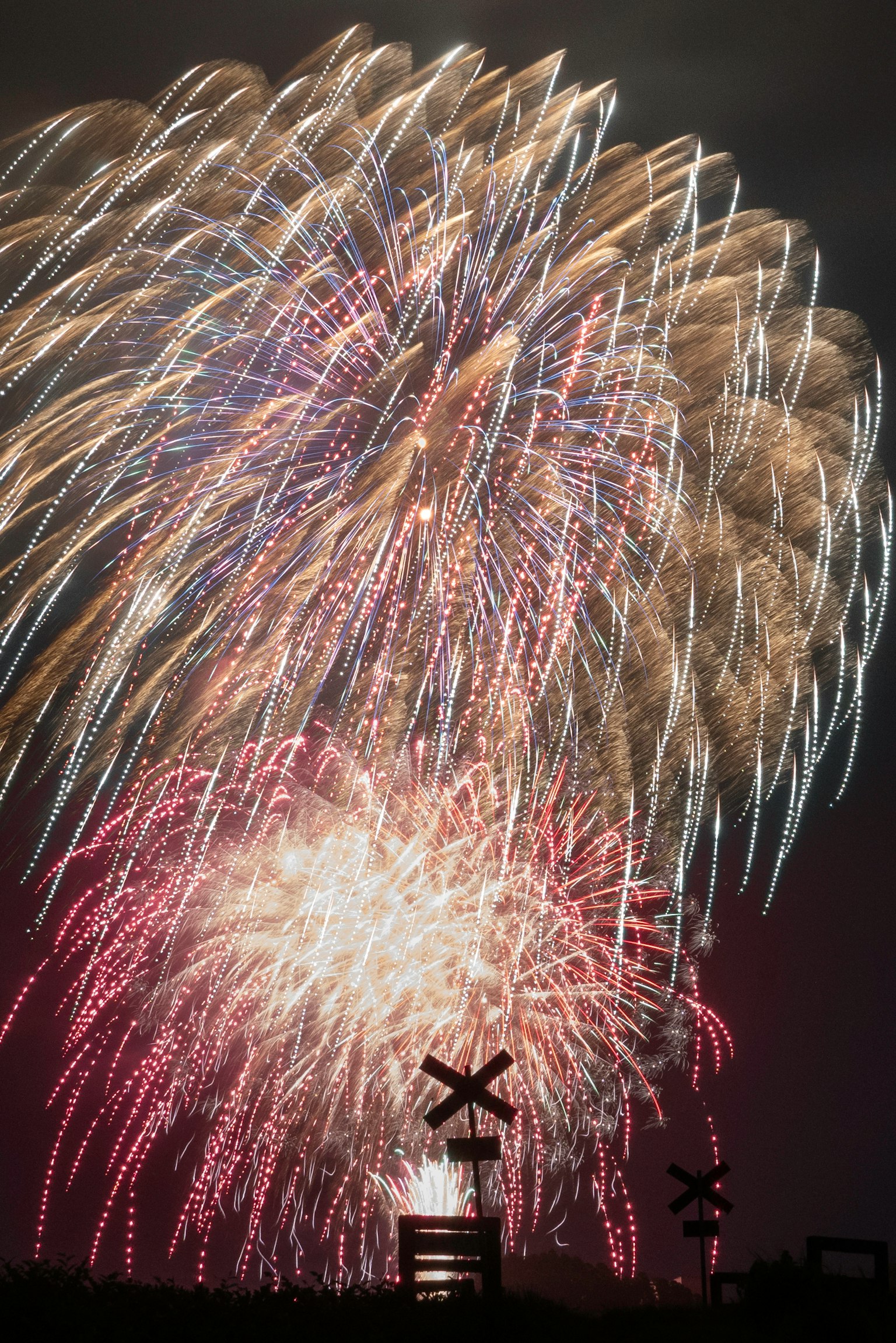 Fuegos artificiales coloridos estallando en el cielo nocturno con objetos en silueta abajo