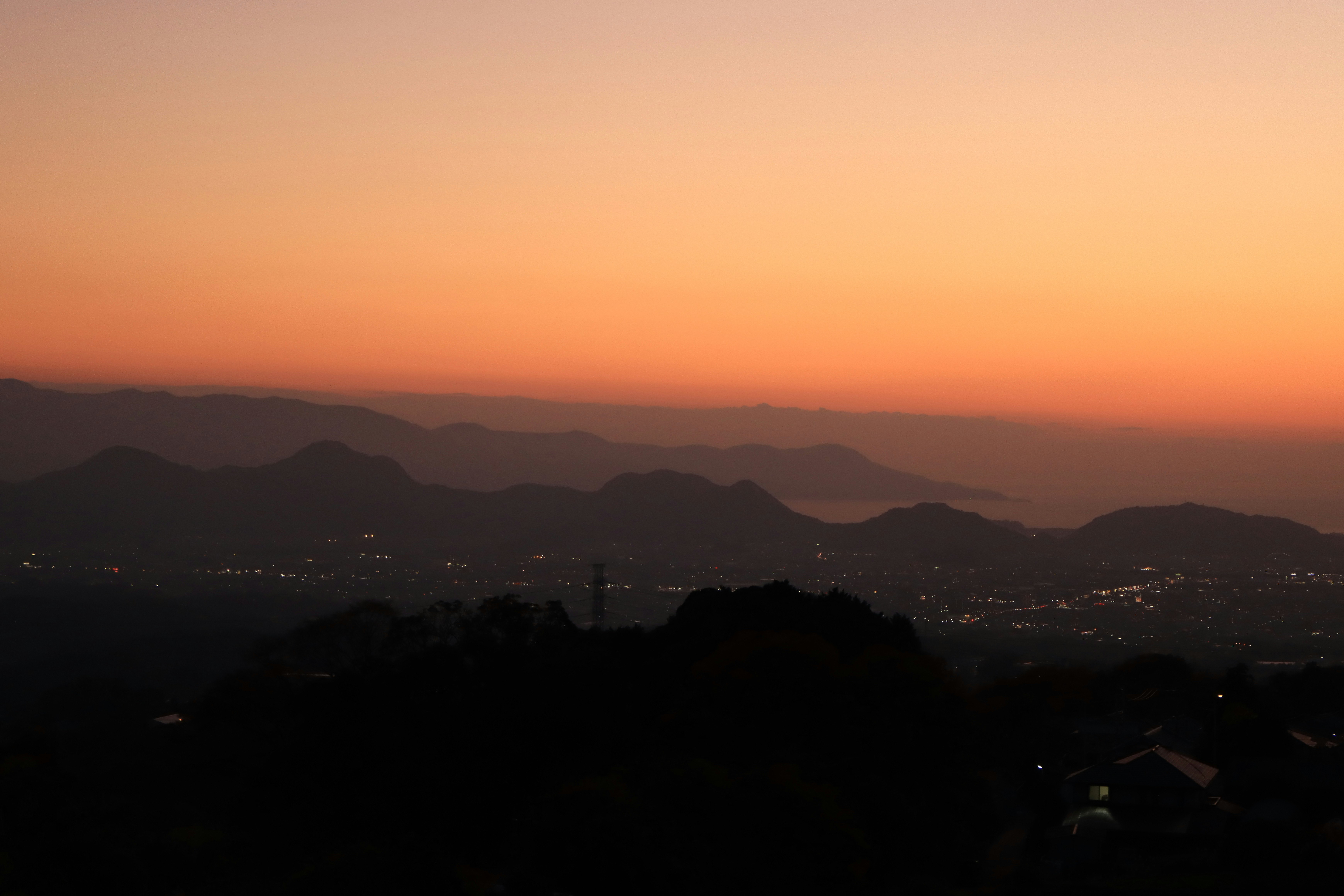 夕暮れの山並みと街の夜景が重なる眺望