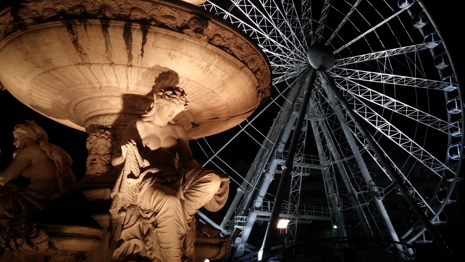 Nachtansicht einer Brunnenskulptur mit einem Riesenrad