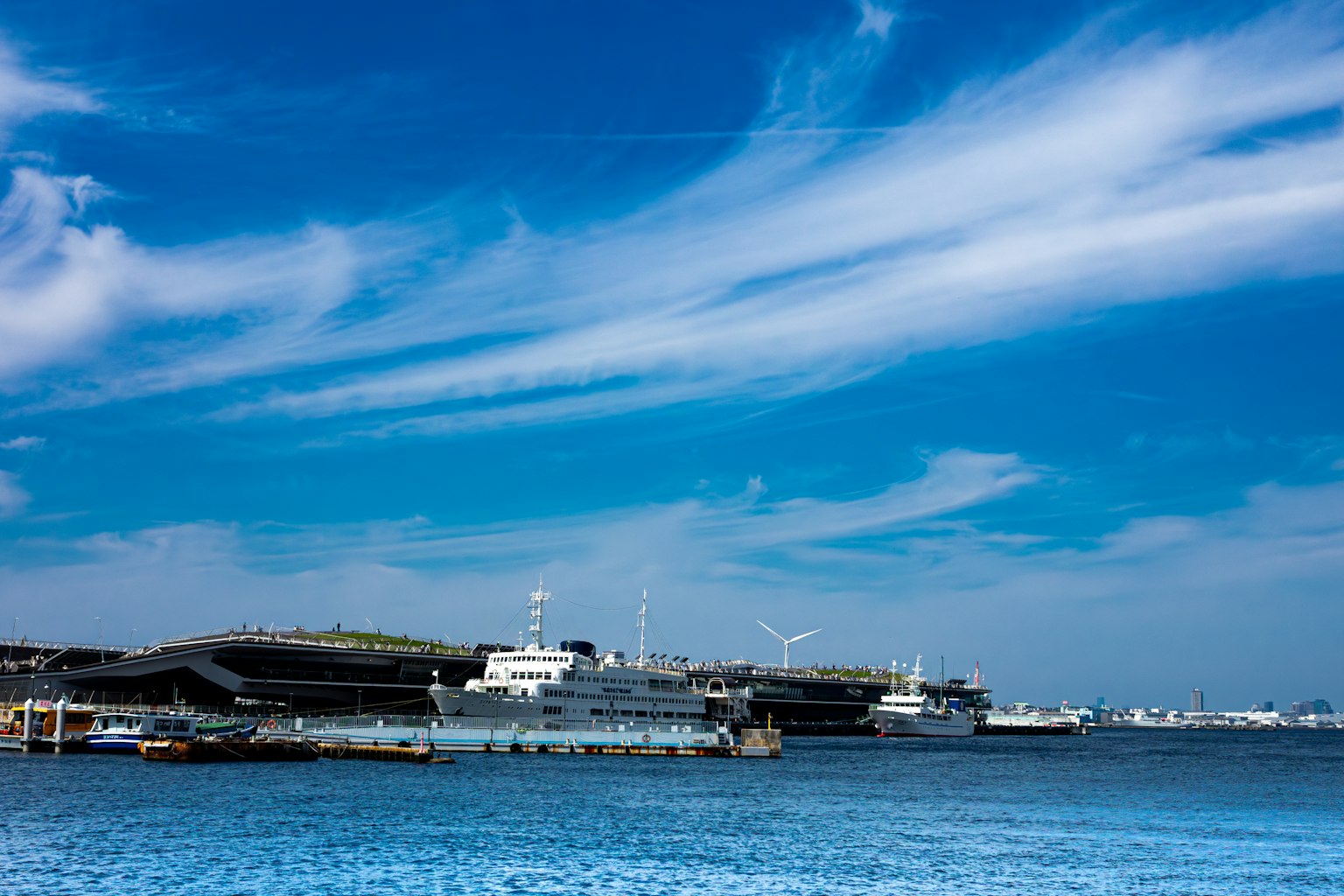 Harbor scene with boats and buildings under a blue sky and clouds