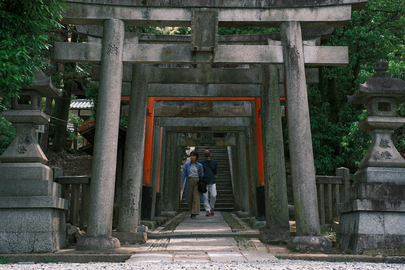 Dos personas caminando a través de un arco de torii con un fondo verde
