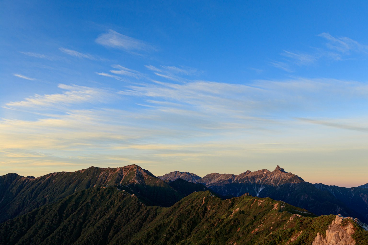 Paisaje montañoso bajo un cielo azul con vegetación exuberante y picos distantes