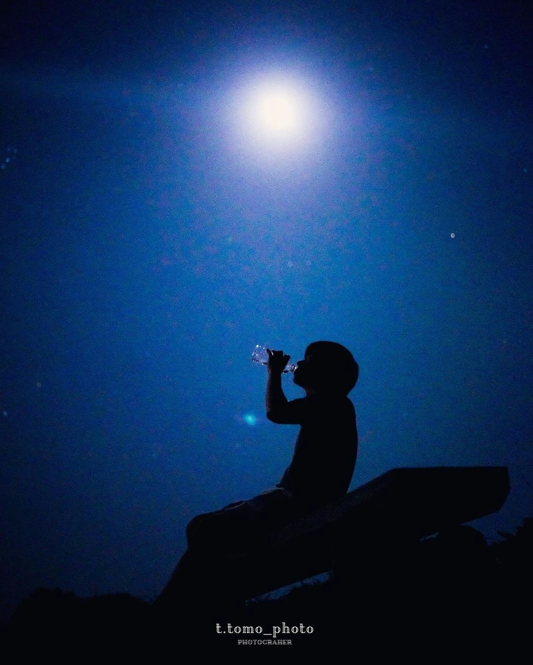 夜空の下で月を見上げるシルエットの人物