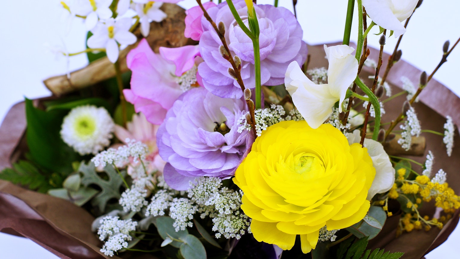 ช่อดอกไม้ที่มีดอกไม้หลากสีรวมถึงกุหลาบสีเหลืองที่โดดเด่นและดอกไม้สีม่วง