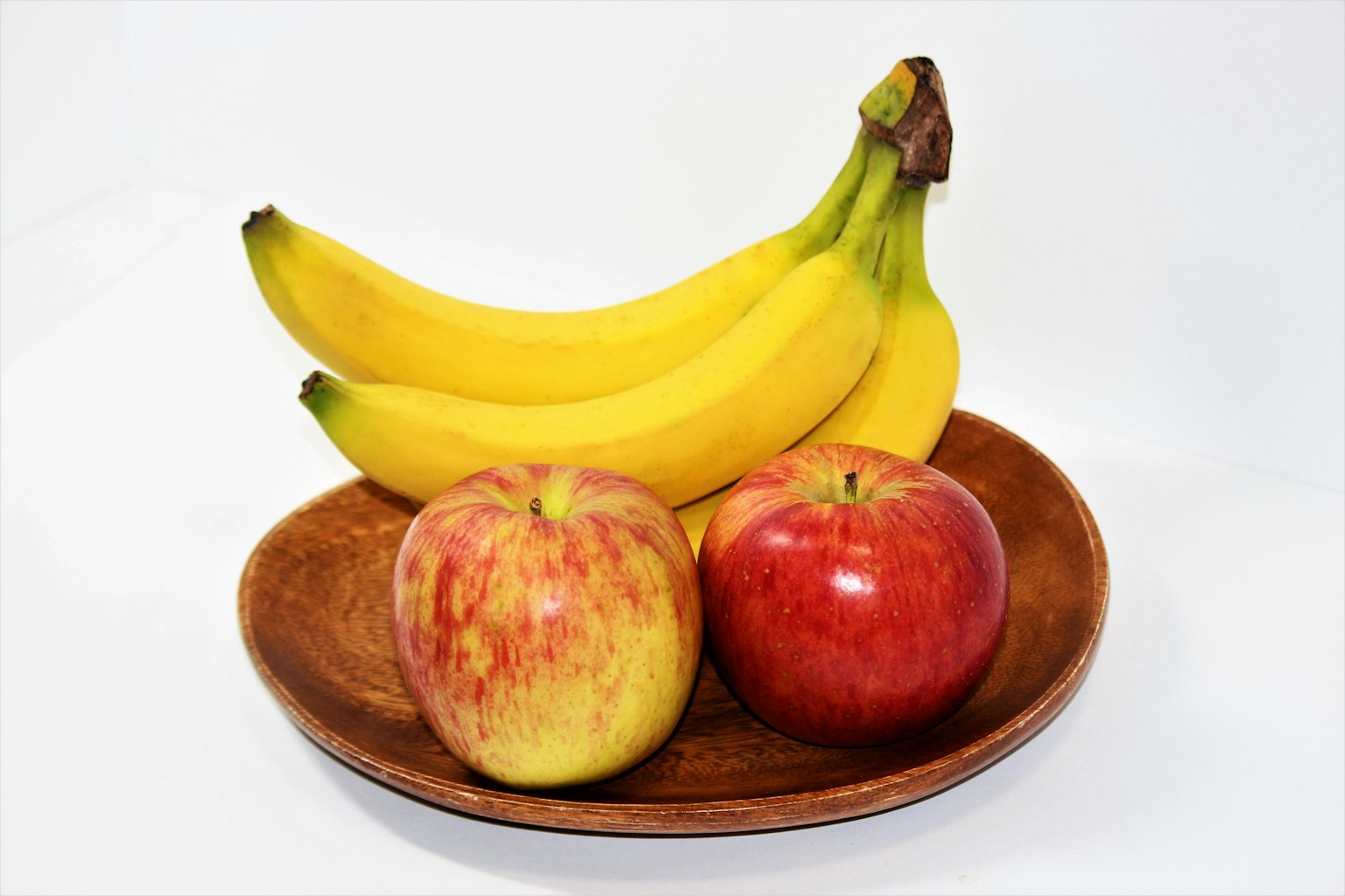 Deux pommes et trois bananes sur une assiette en bois