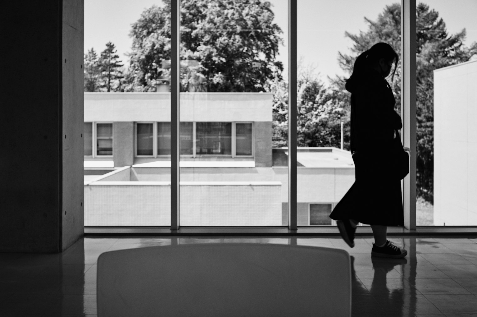 Silhouette einer Frau, die neben einem Fenster mit moderner Architektur im Hintergrund geht