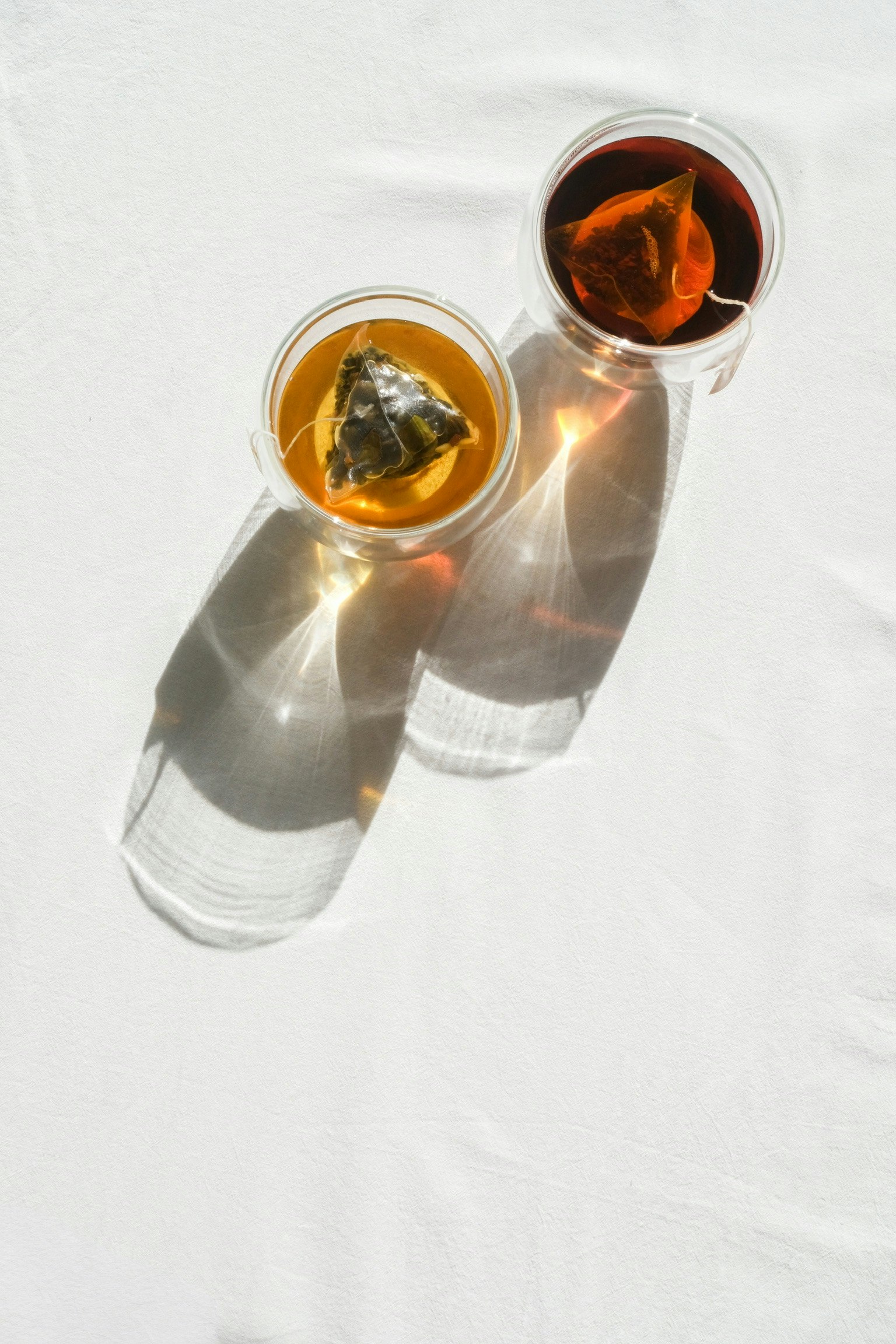 Deux tasses transparentes contenant du thé vert et du thé noir sur une surface blanche