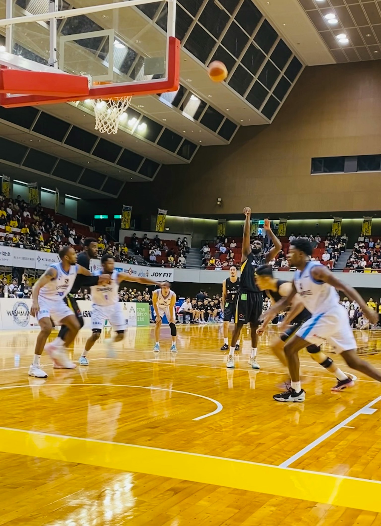 Juego de baloncesto con jugadores lanzando mientras los espectadores observan