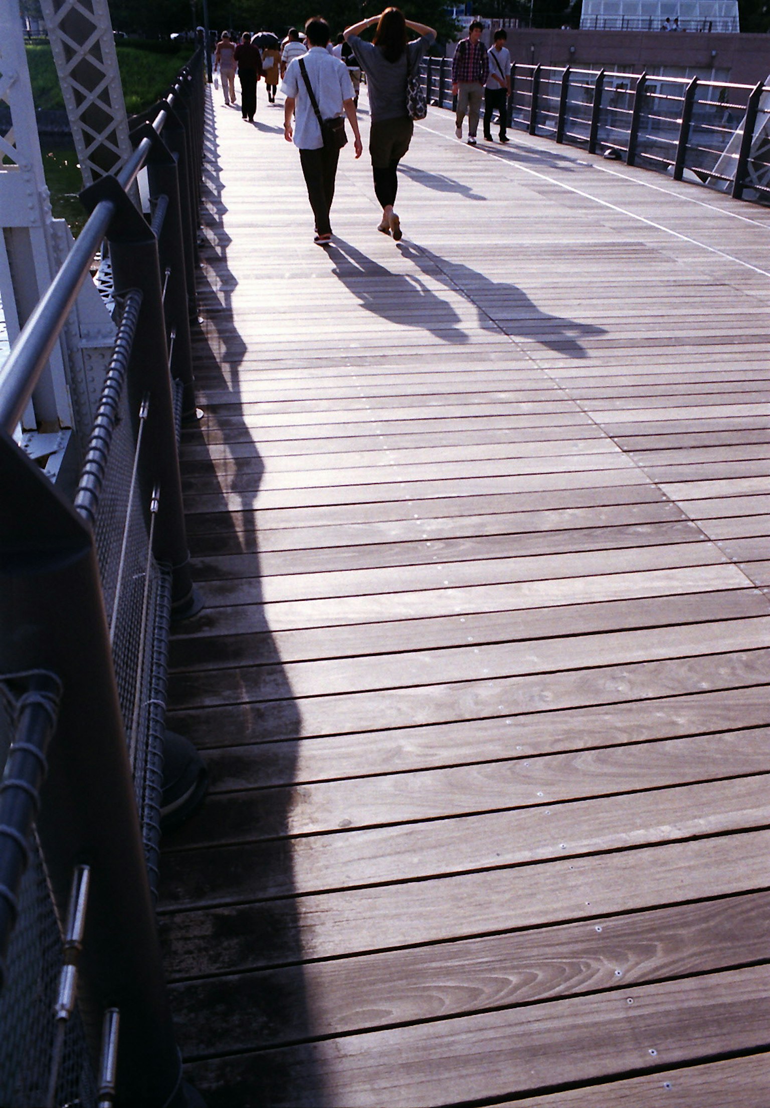 Menschen gehen über eine Holzbrücke mit Schatten auf den Planken