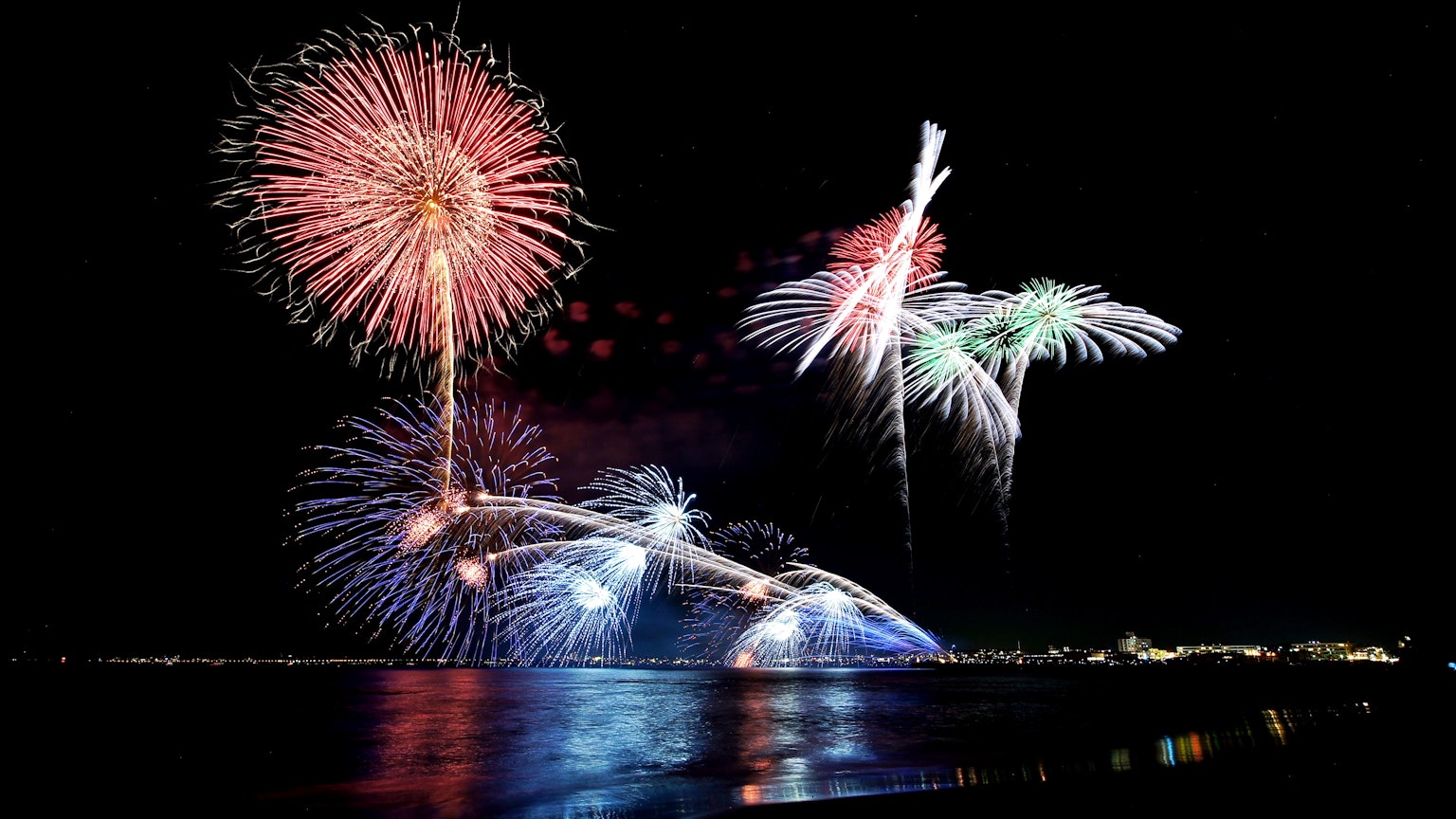 Spettacolo di fuochi d'artificio colorati che si riflettono sull'acqua di notte
