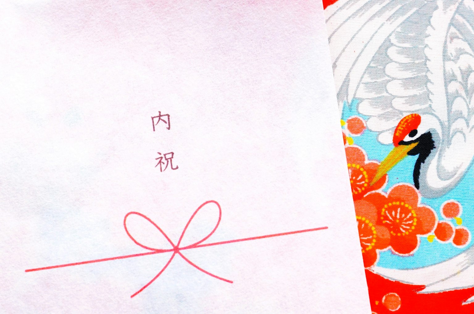 Une enveloppe blanche avec un ruban rouge portant le texte 内祝 et un design de grue coloré