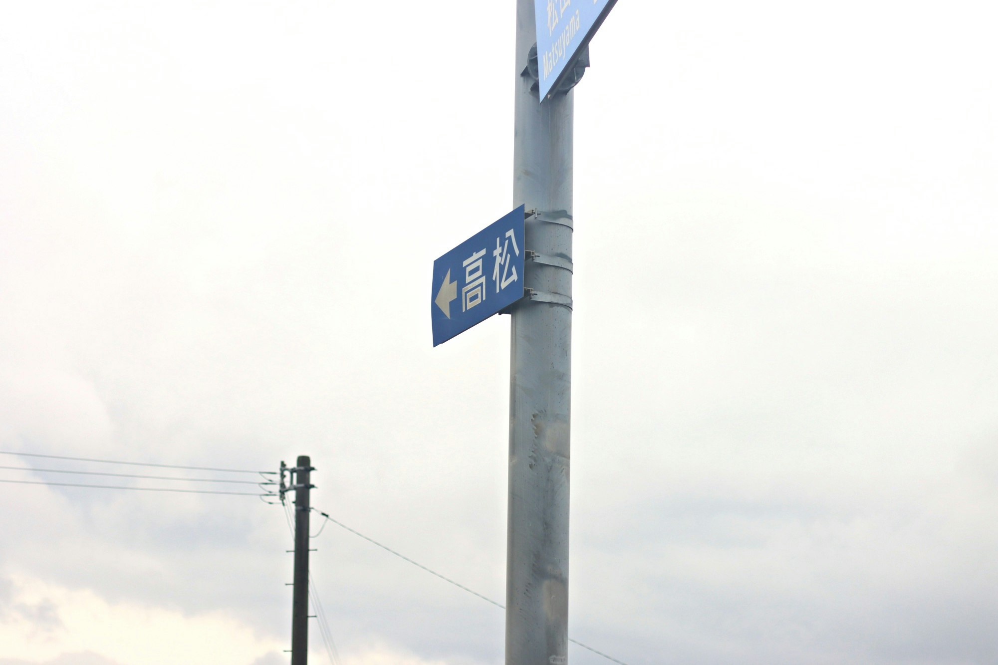空に向かう電柱と「高砂」表示の青い標識のある街角