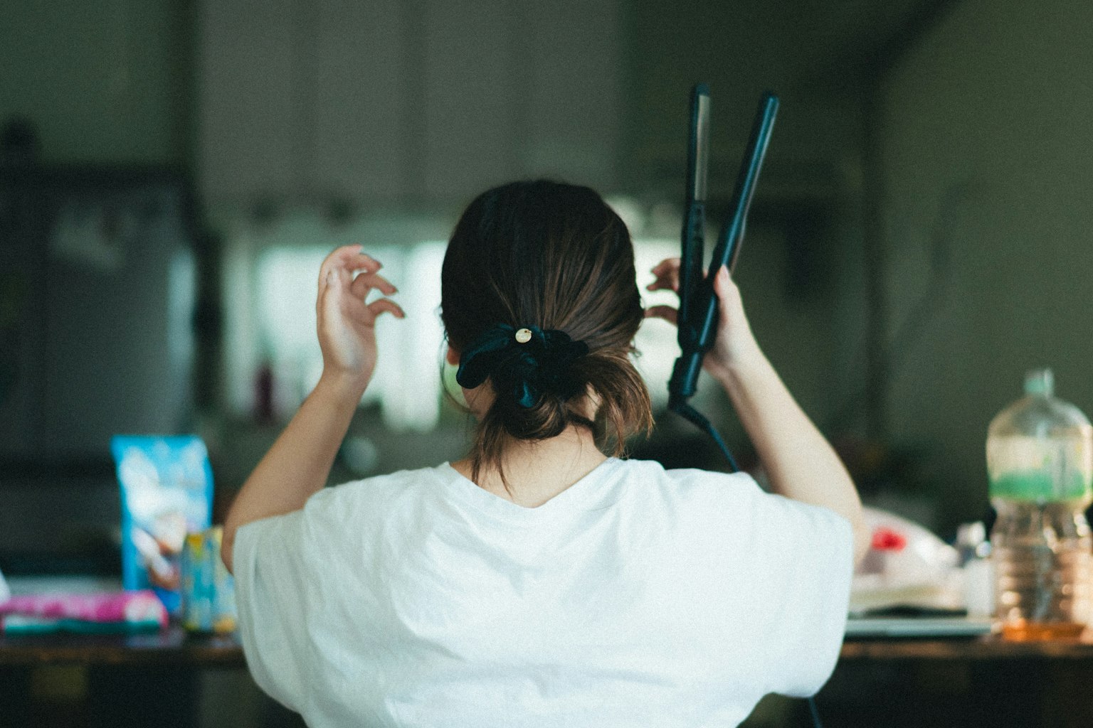 女性がヘアアイロンを持ち髪を整えている後ろ姿