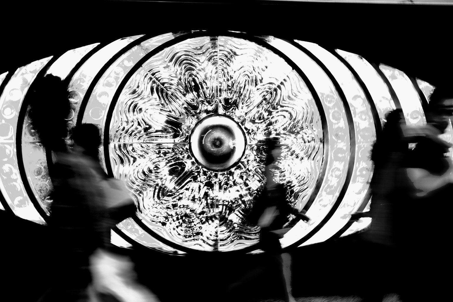 People walking in front of a large eye design on a black and white wall