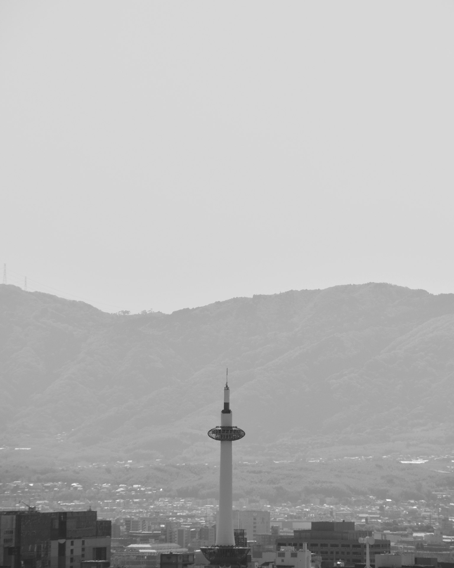 Paesaggio urbano in bianco e nero con una torre e montagne sullo sfondo