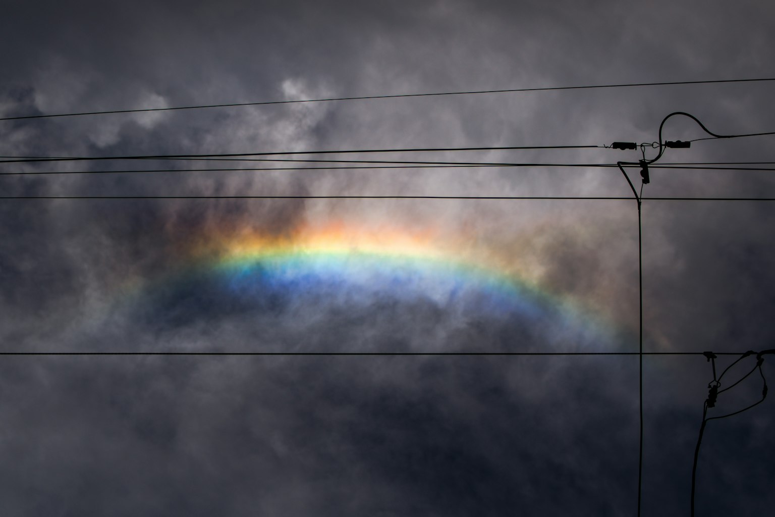Ein Regenbogen, der zwischen dunklen Wolken mit Stromleitungen erscheint