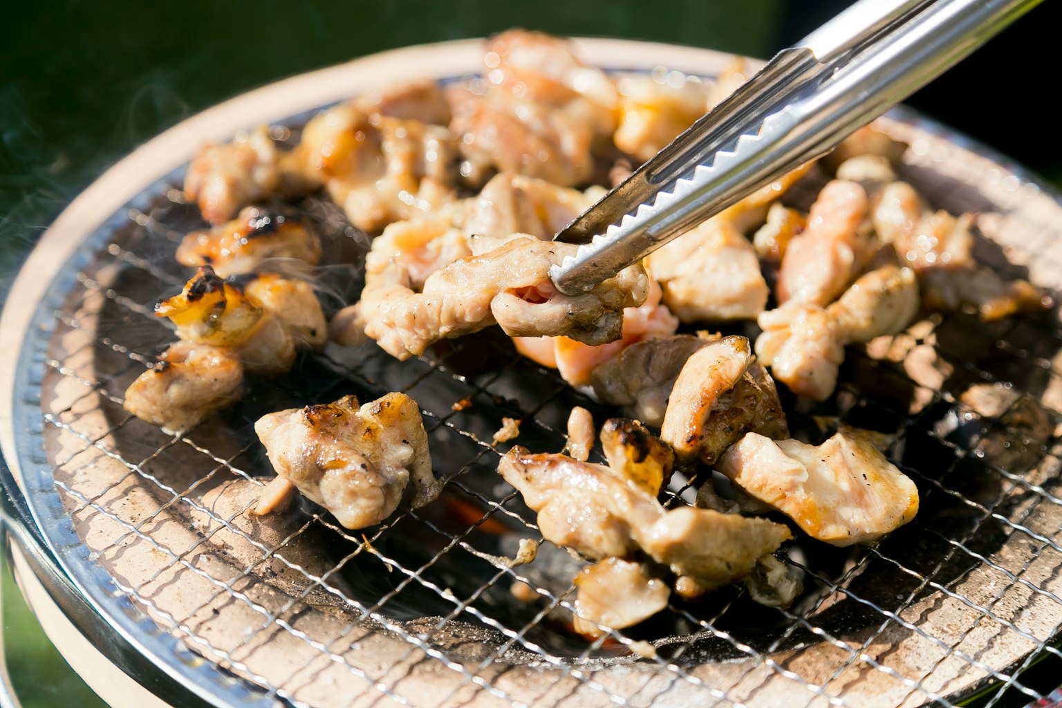 Grilled chicken pieces on a wire mesh with tongs lifting some