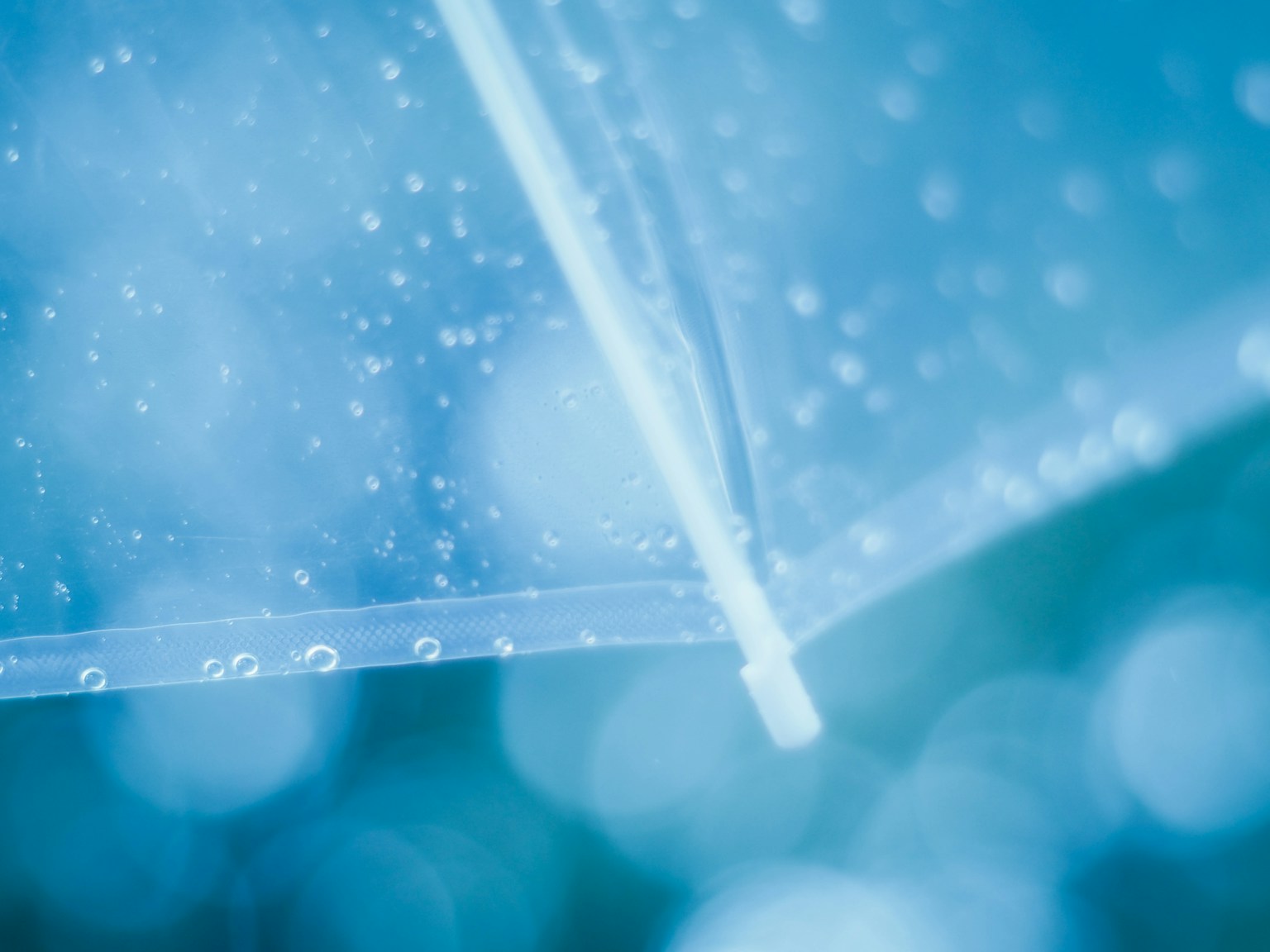 透明雨傘的特寫，水滴附著在藍色背景上