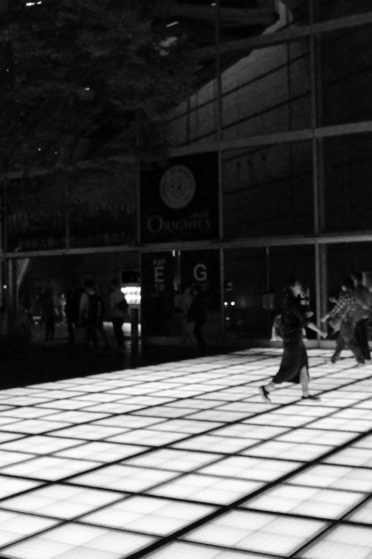 Des personnes marchant sur un sol lumineux dans un fond noir et blanc