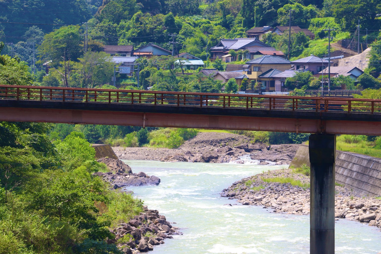 Pont sur une rivière avec des maisons et des collines verdoyantes en arrière-plan