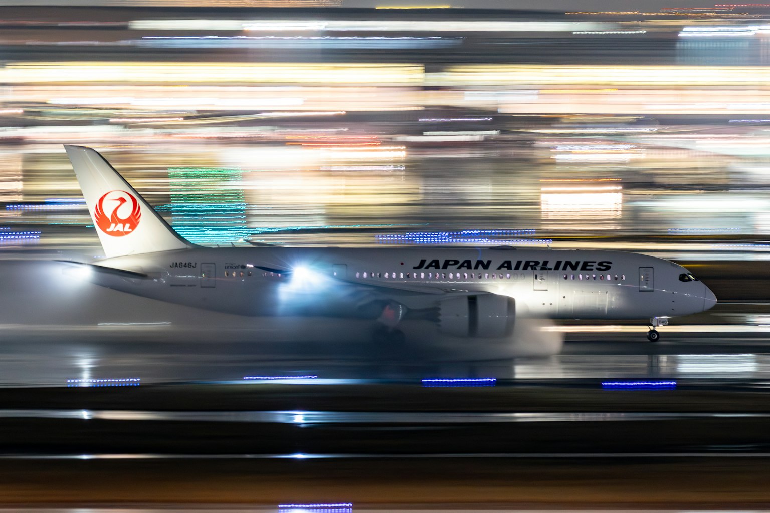Avion Japan Airlines roulant sur la piste la nuit avec des lumières floues
