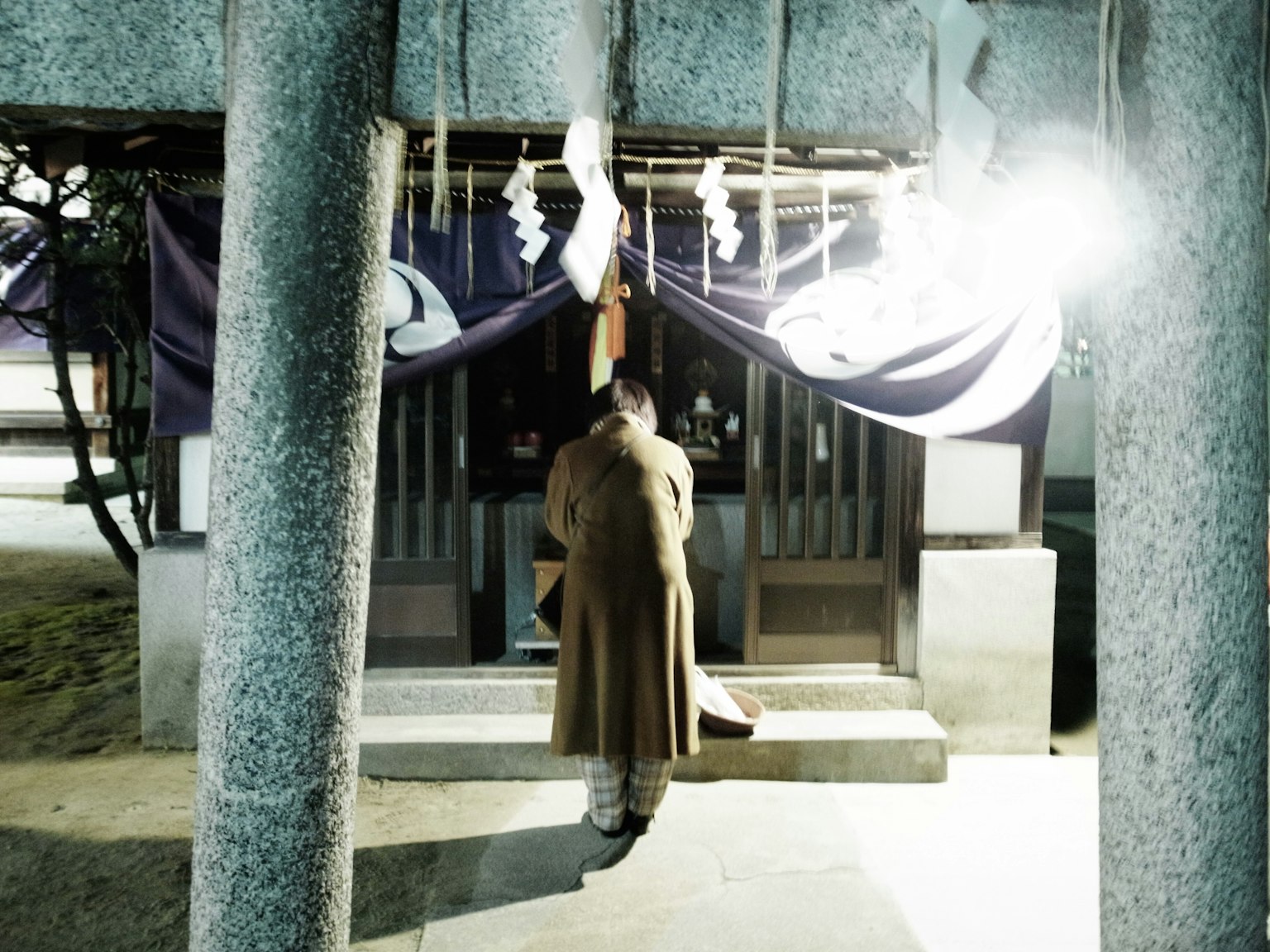 A figure standing before a shrine at night with illuminated entrance and decorations