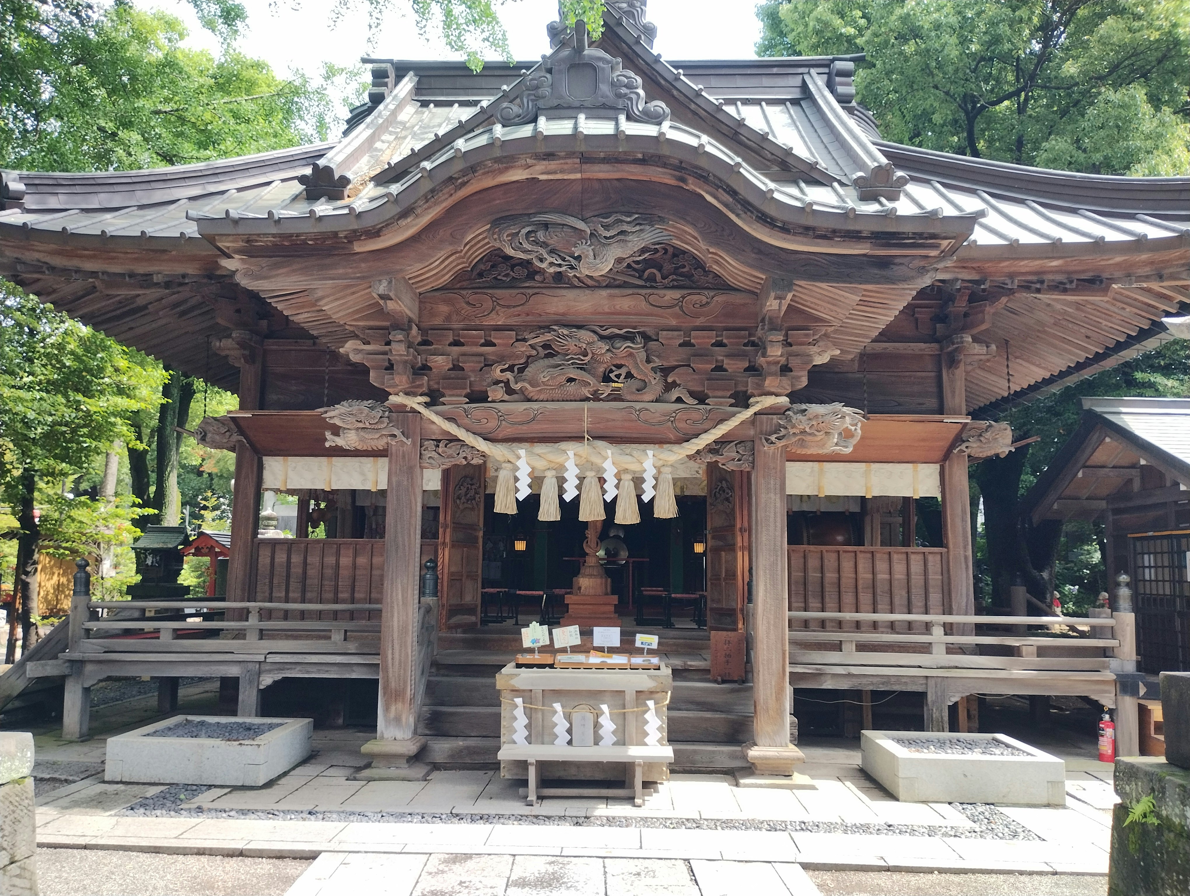 木造の神社本殿と拝殿、注連縄と鈴のある祭壇