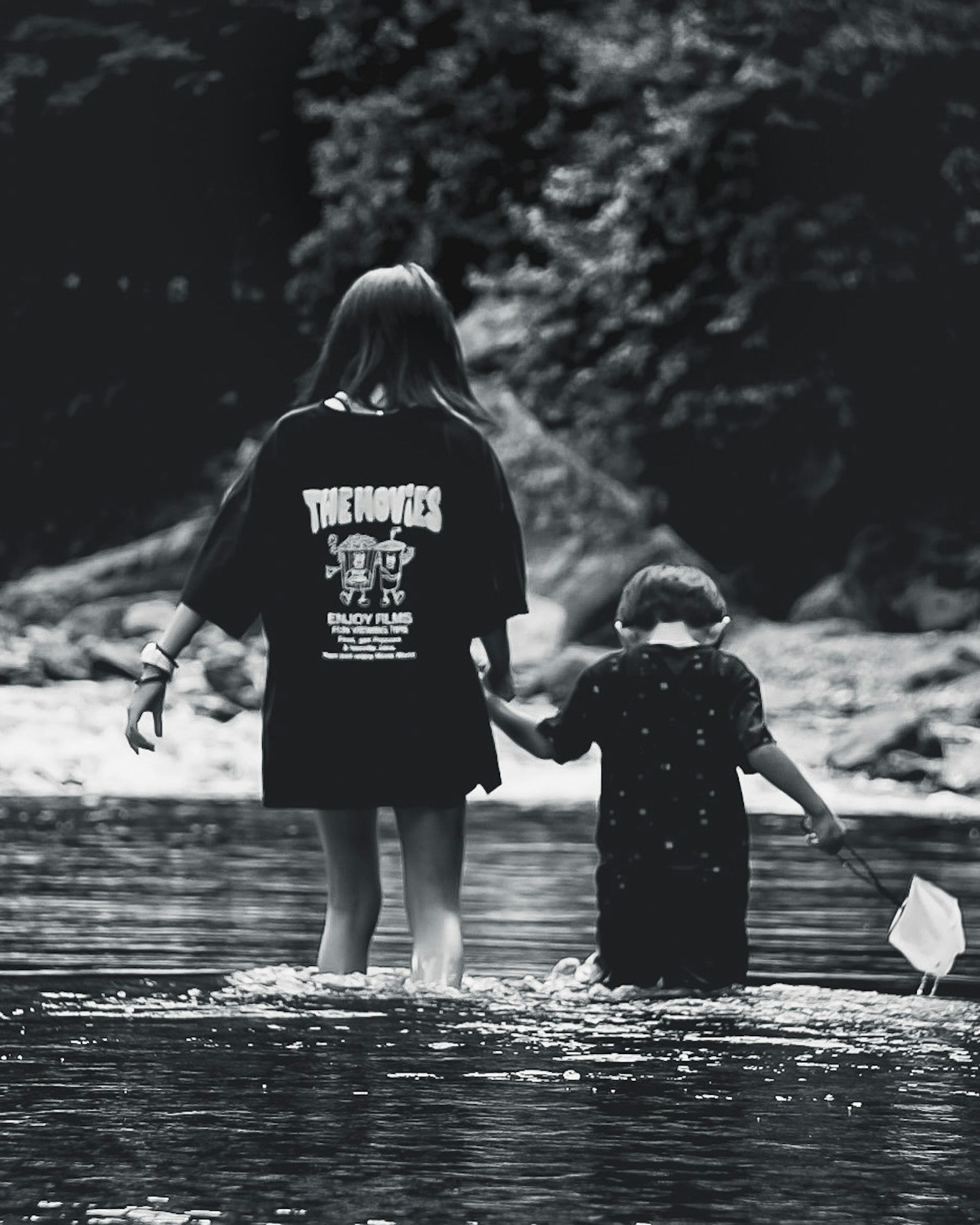 Foto in bianco e nero di una ragazza che cammina in un fiume tenendo per mano un bambino