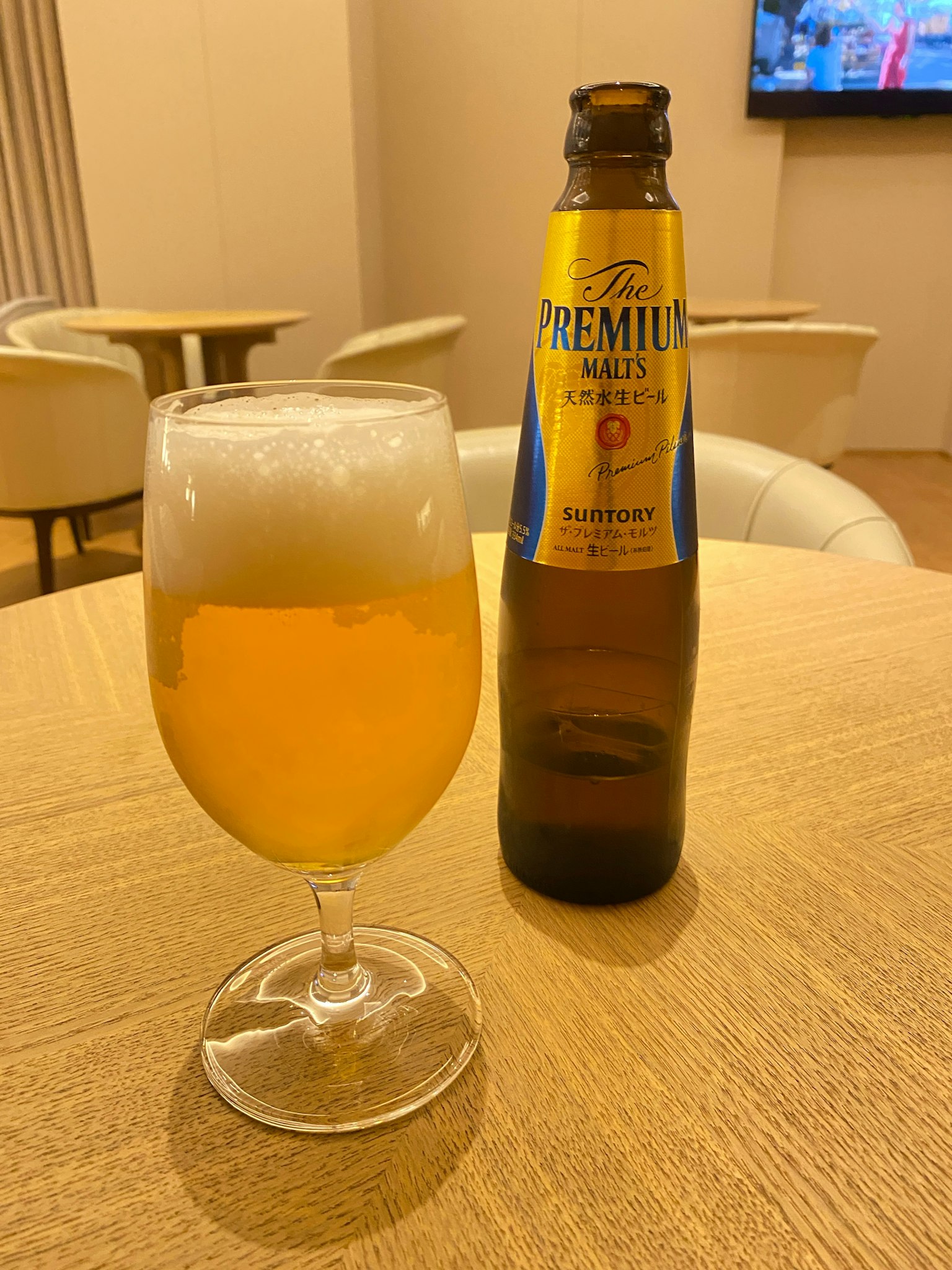 Segelas bir berbusa dan sebuah botol di atas meja kayu