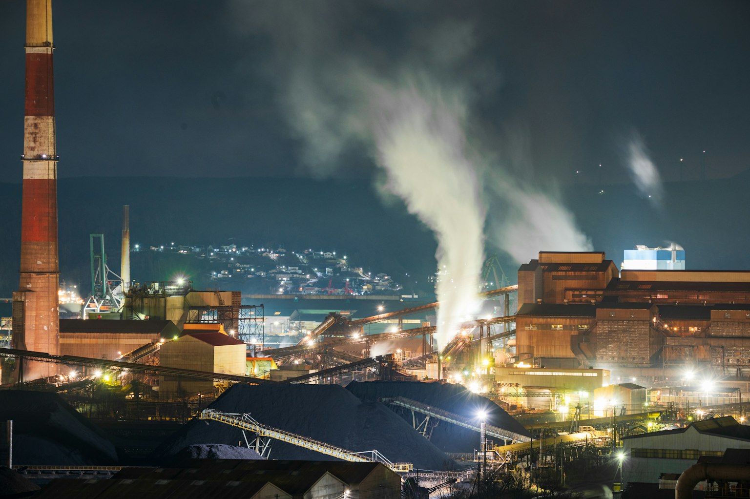 Industrielandschaft bei Nacht mit Rauch aus Schornsteinen und Fabriken