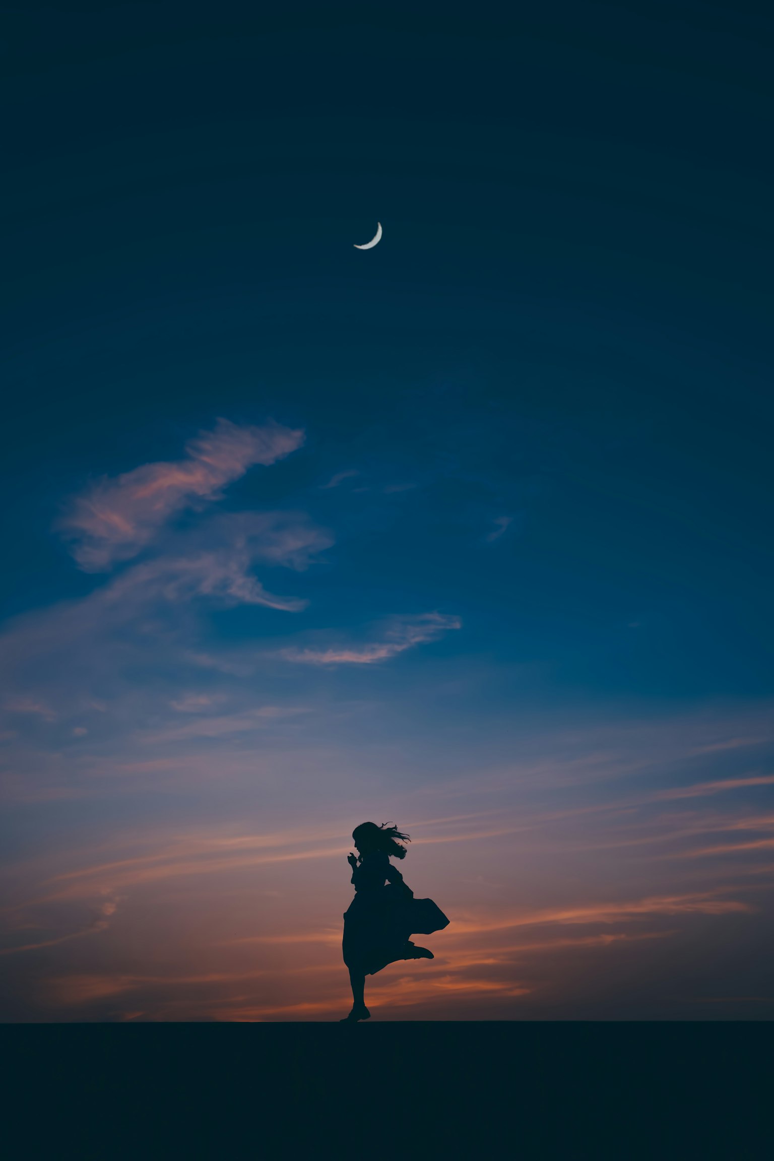 Silhouette d'une femme tournant dans une jupe sous un ciel crépusculaire avec une lune croissante