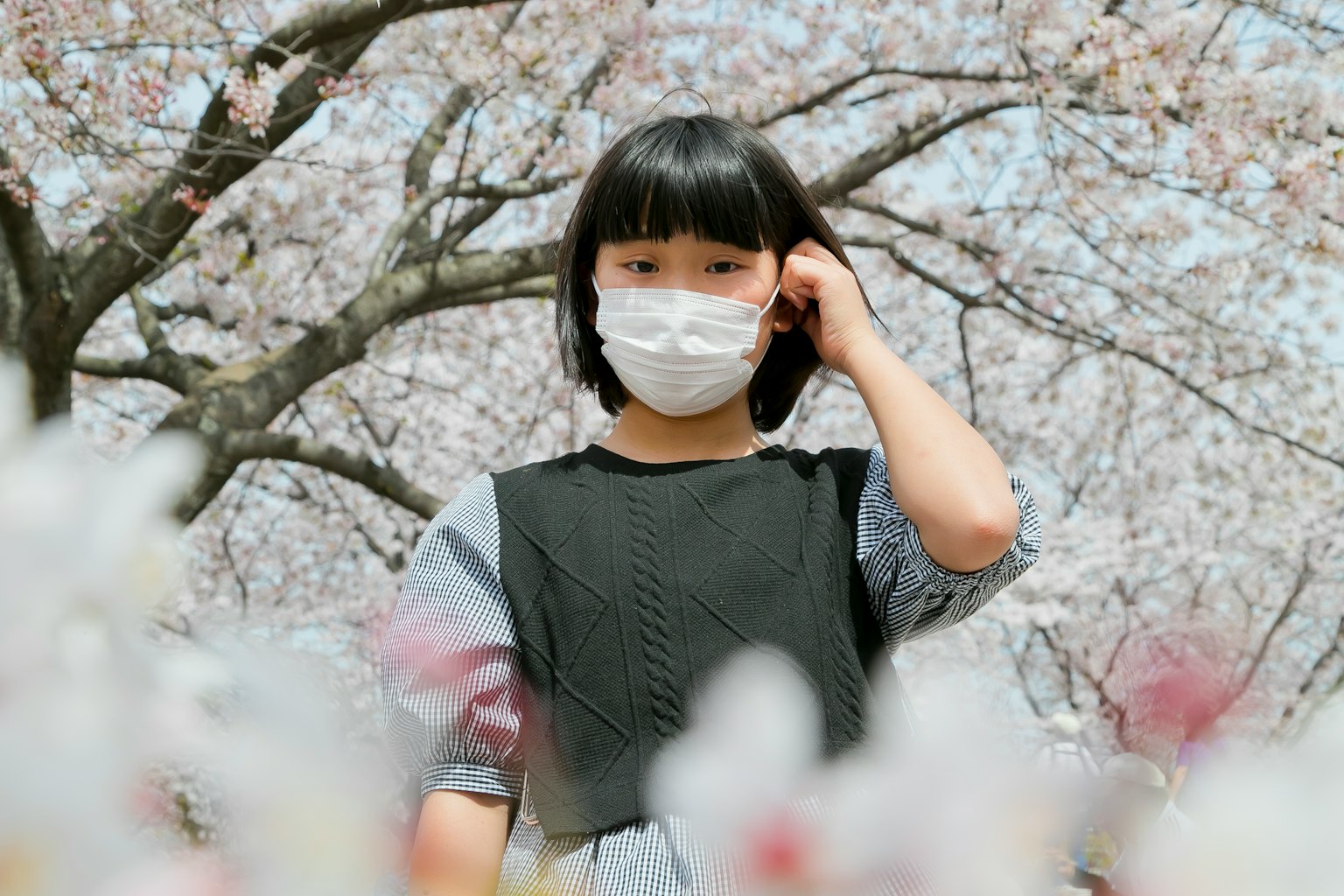 Girl wearing a mask standing in front of cherry blossoms