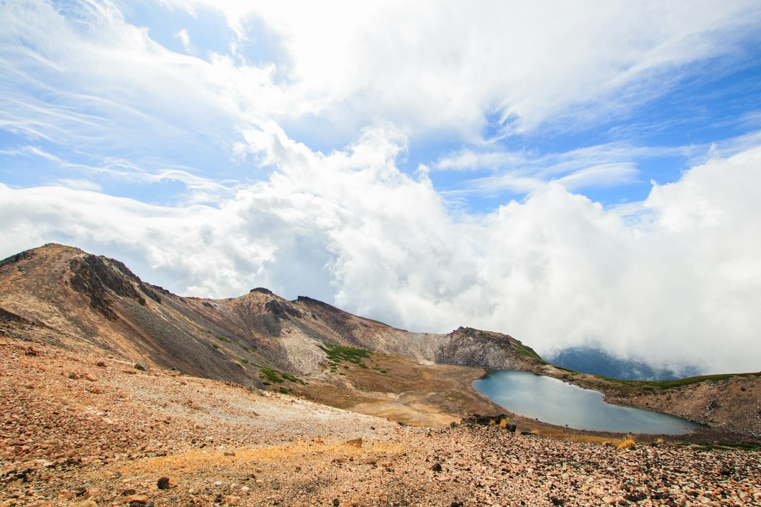 Paesaggio di cratere vulcanico con lago cielo sereno e contrasto di nuvole