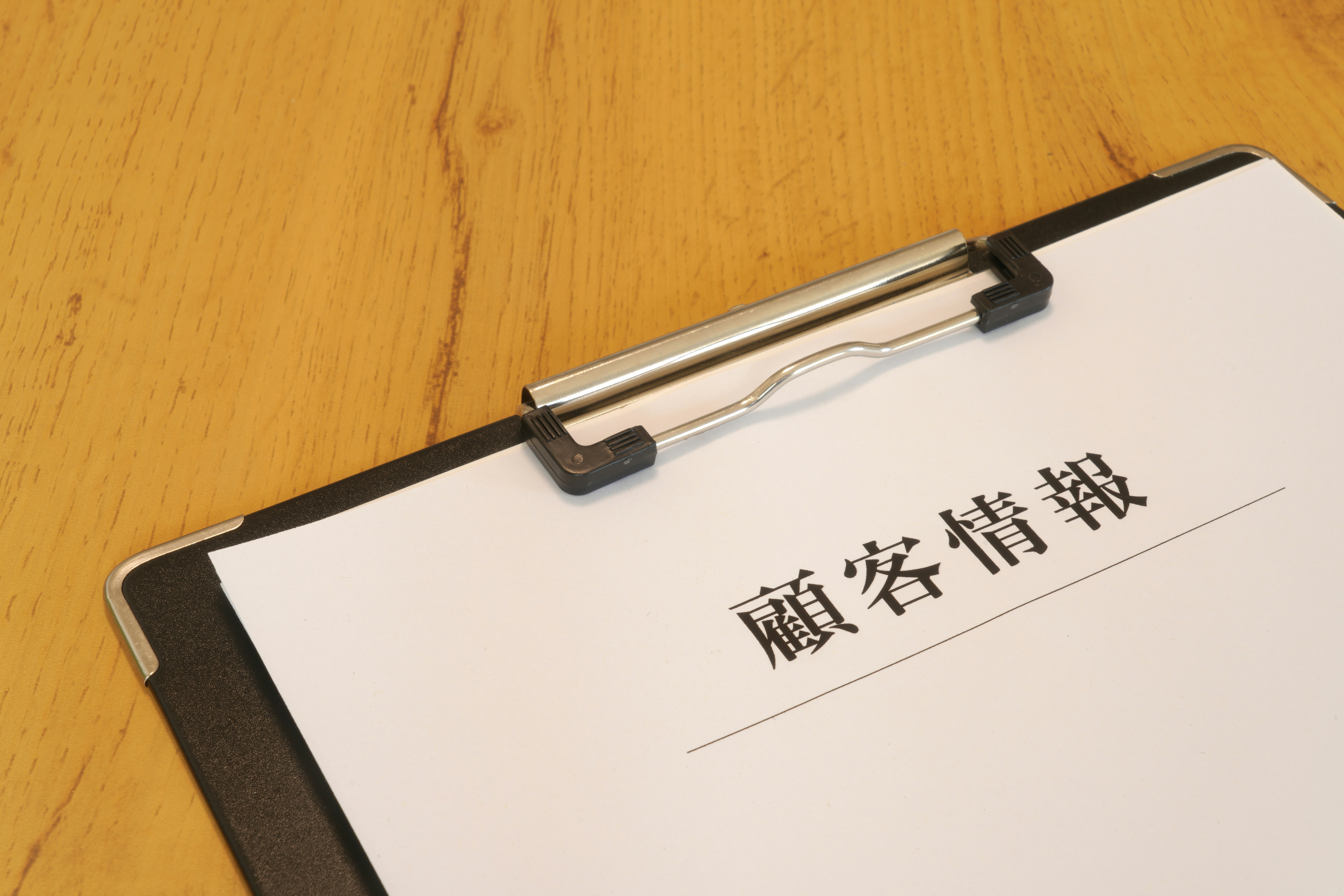 木の机の上に置かれた書類とクリップボードの文字