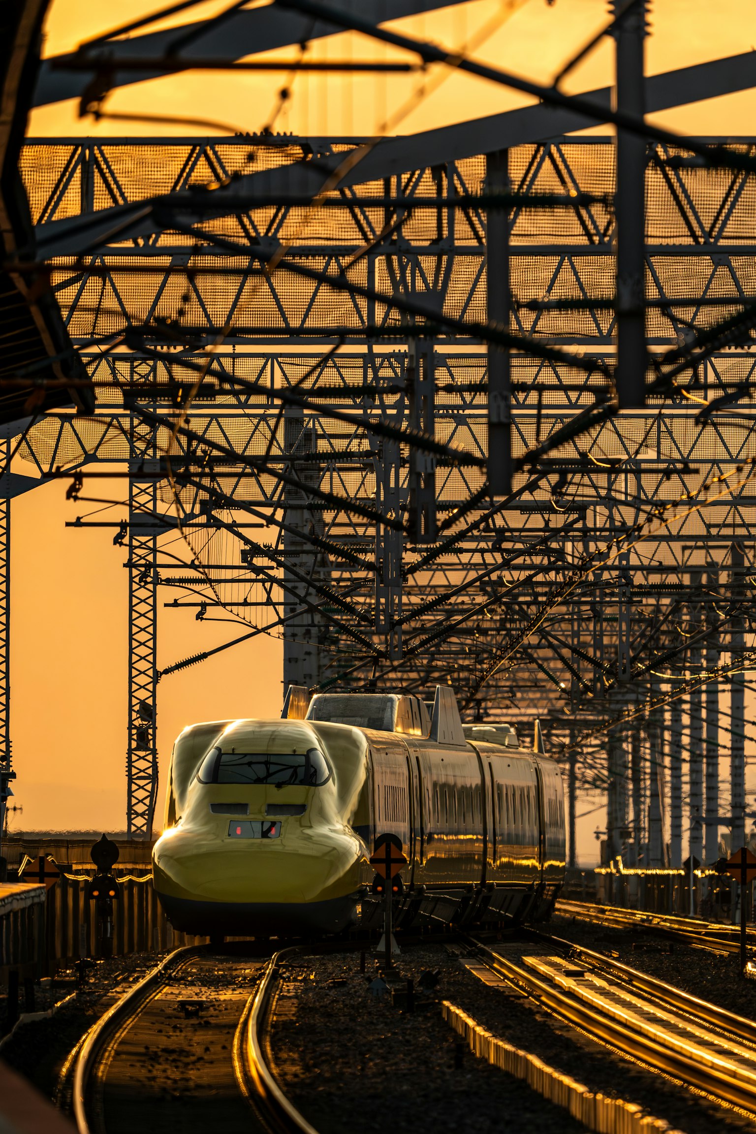 รถไฟชินกันเซนสีเหลืองในยามพระอาทิตย์ตกพร้อมโครงสร้างราง